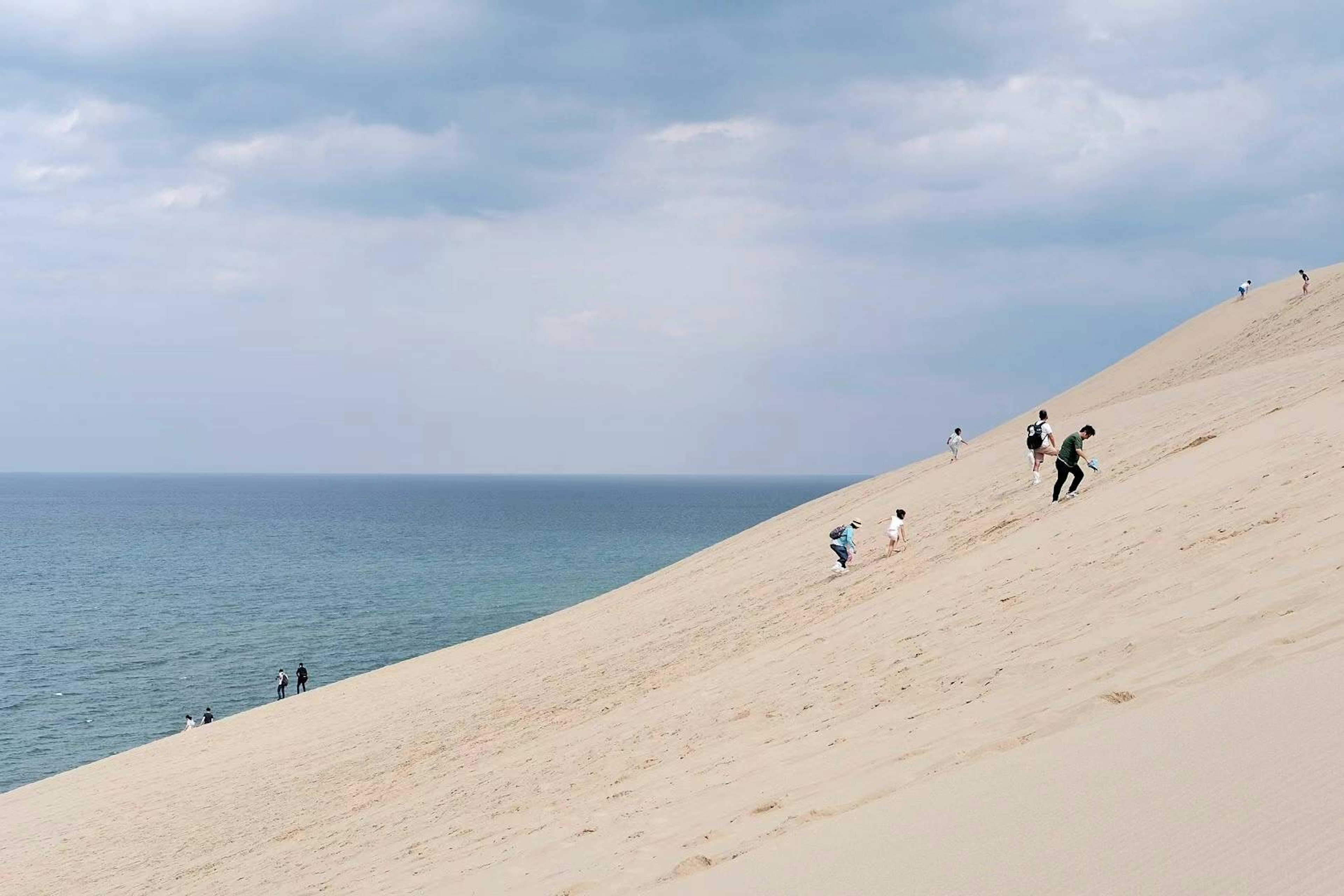 Personas subiendo dunas de arena con un océano azul al fondo