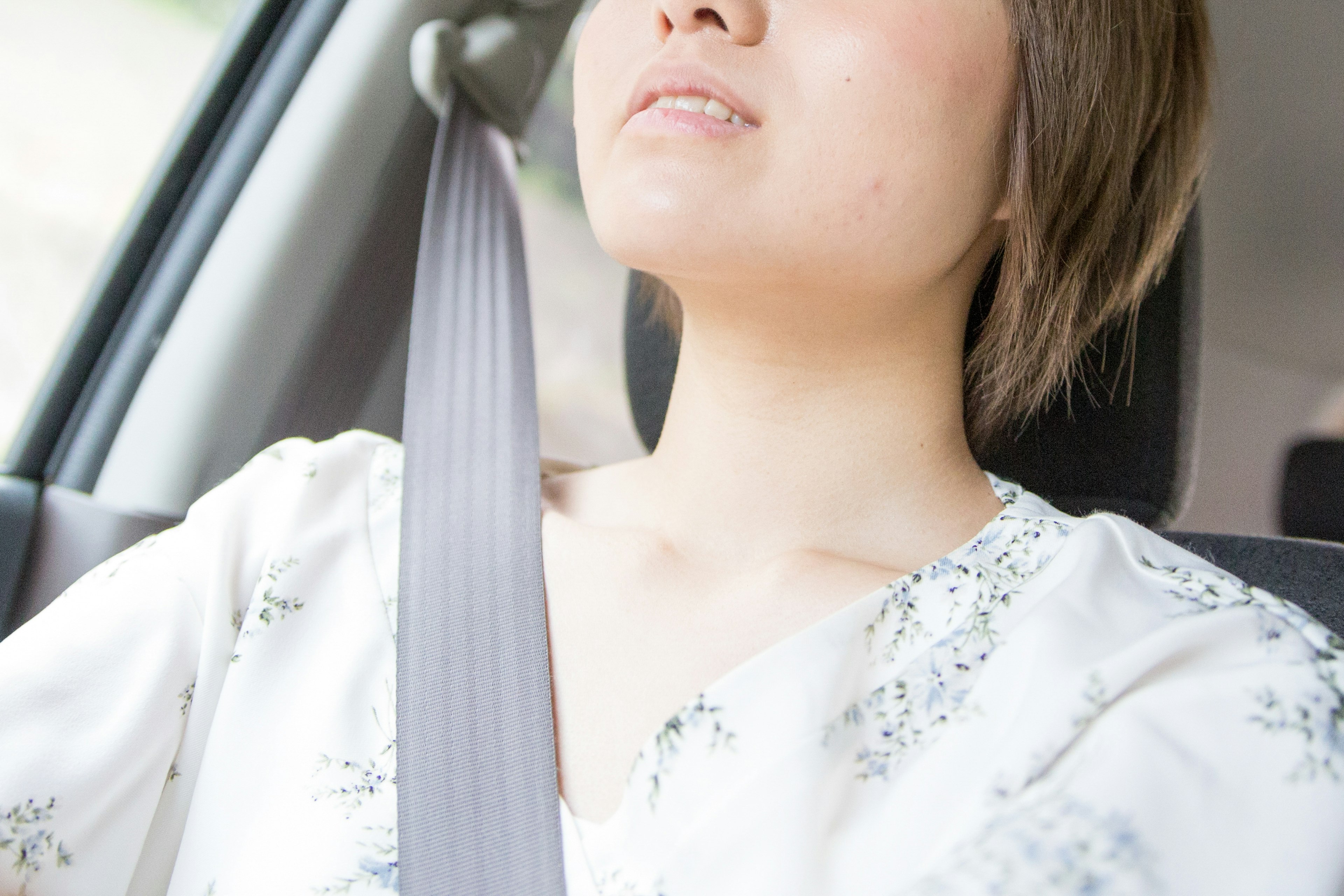 運転中の女性の上半身が見える画像でシートベルトを着用し白いブラウスを着ている