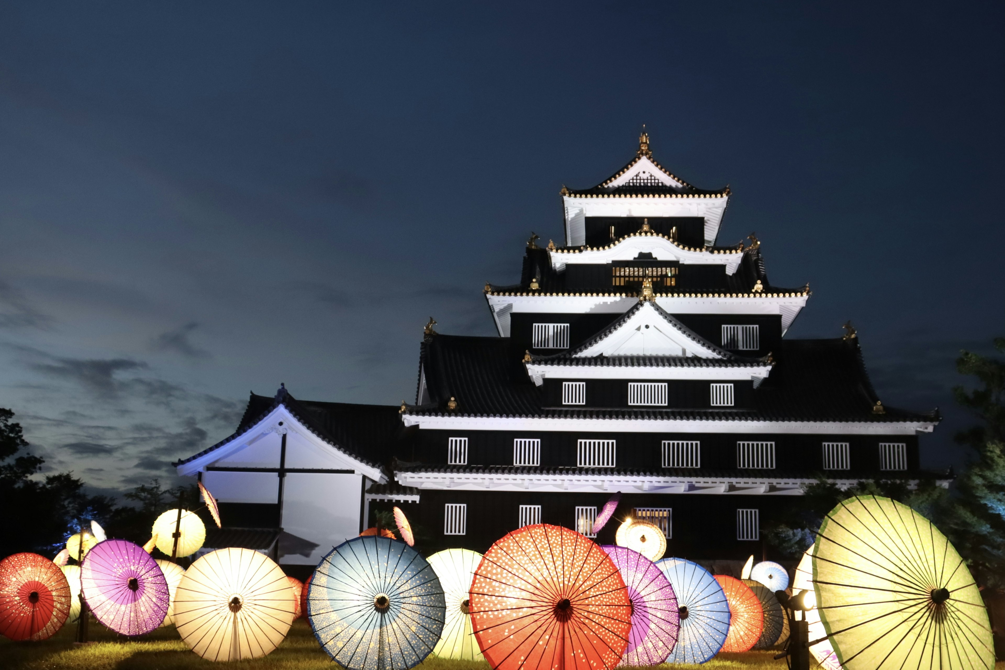 Bunte Regenschirme vor einem traditionellen japanischen Schloss bei Nacht