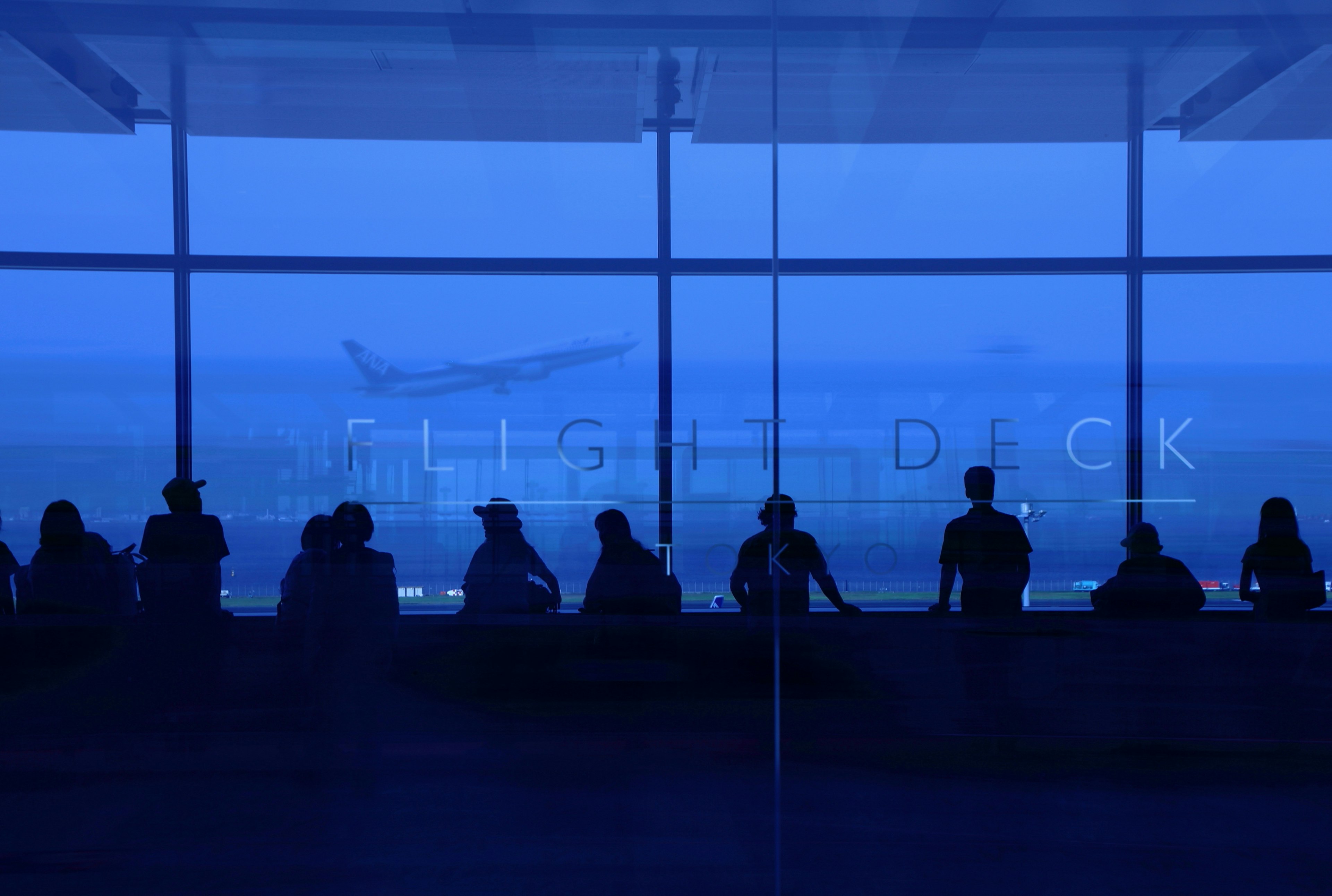 Silhouetten von Menschen auf dem Flugdeck eines Flughafens vor blauem Hintergrund