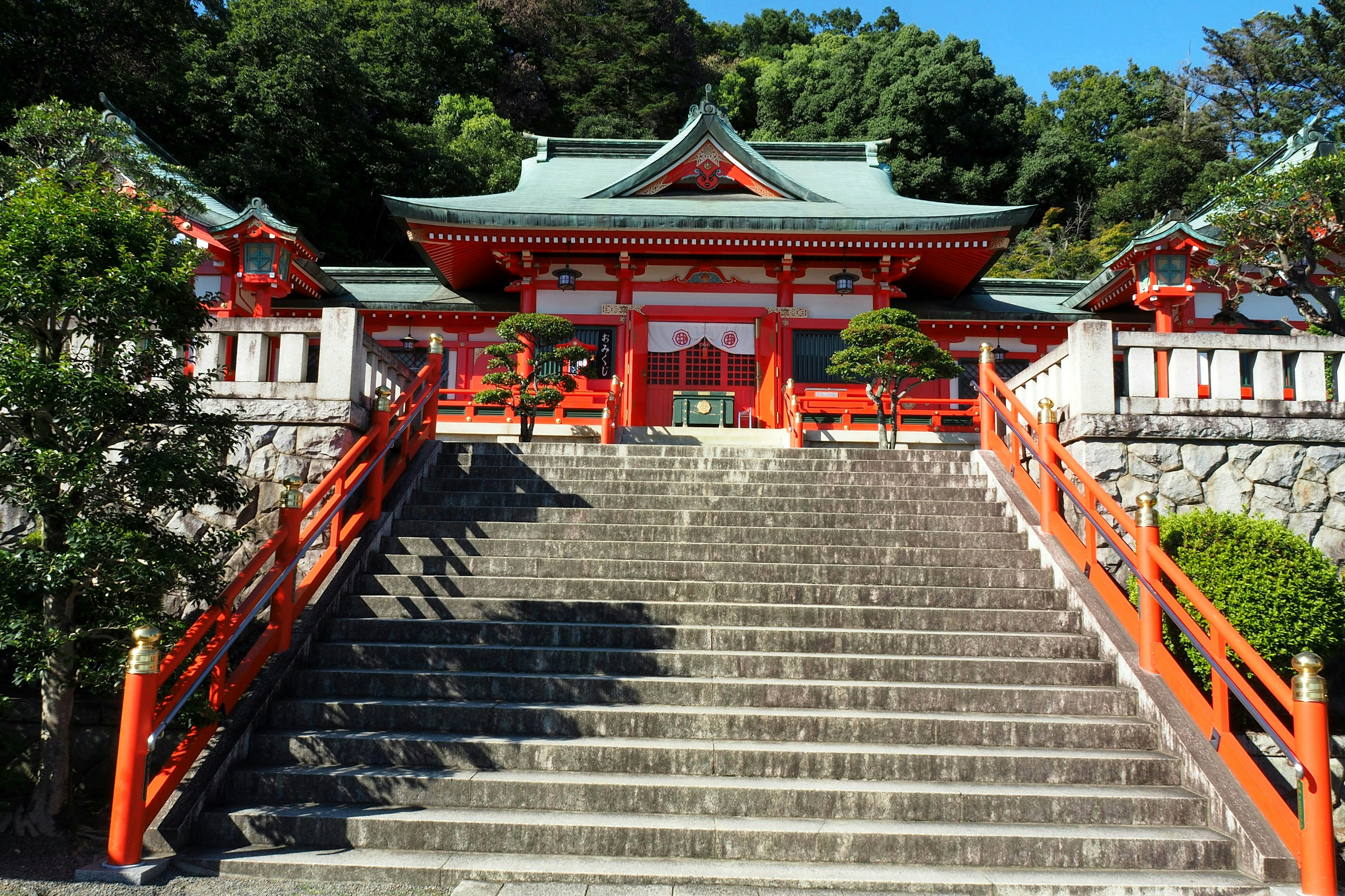 Stairs leading to a vibrant red shrine surrounded by greenery