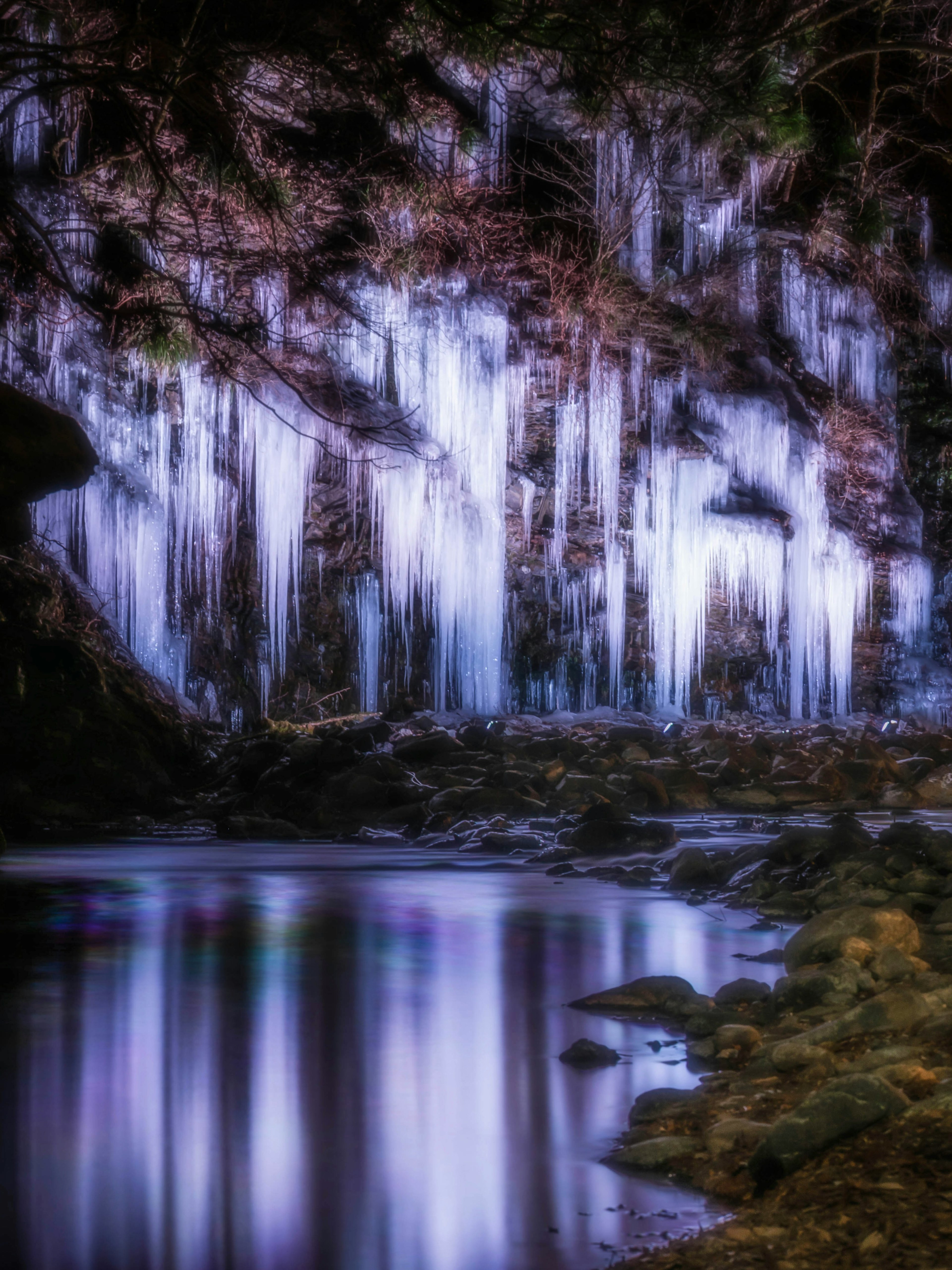 A stunning landscape featuring icicles hanging from a waterfall with reflections in the water