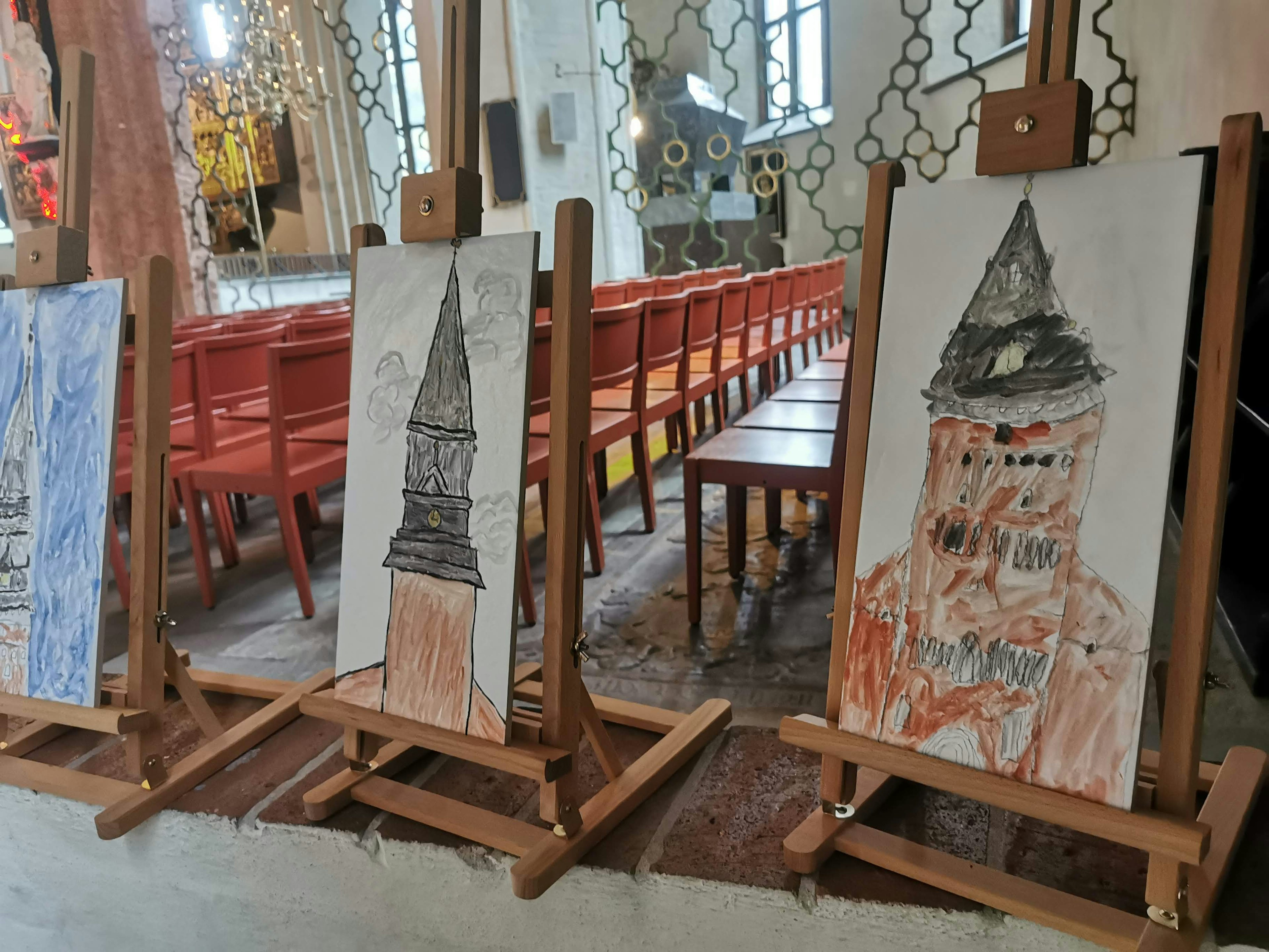 Trois dessins d'enfants exposés sur des chevalets à l'intérieur d'une église