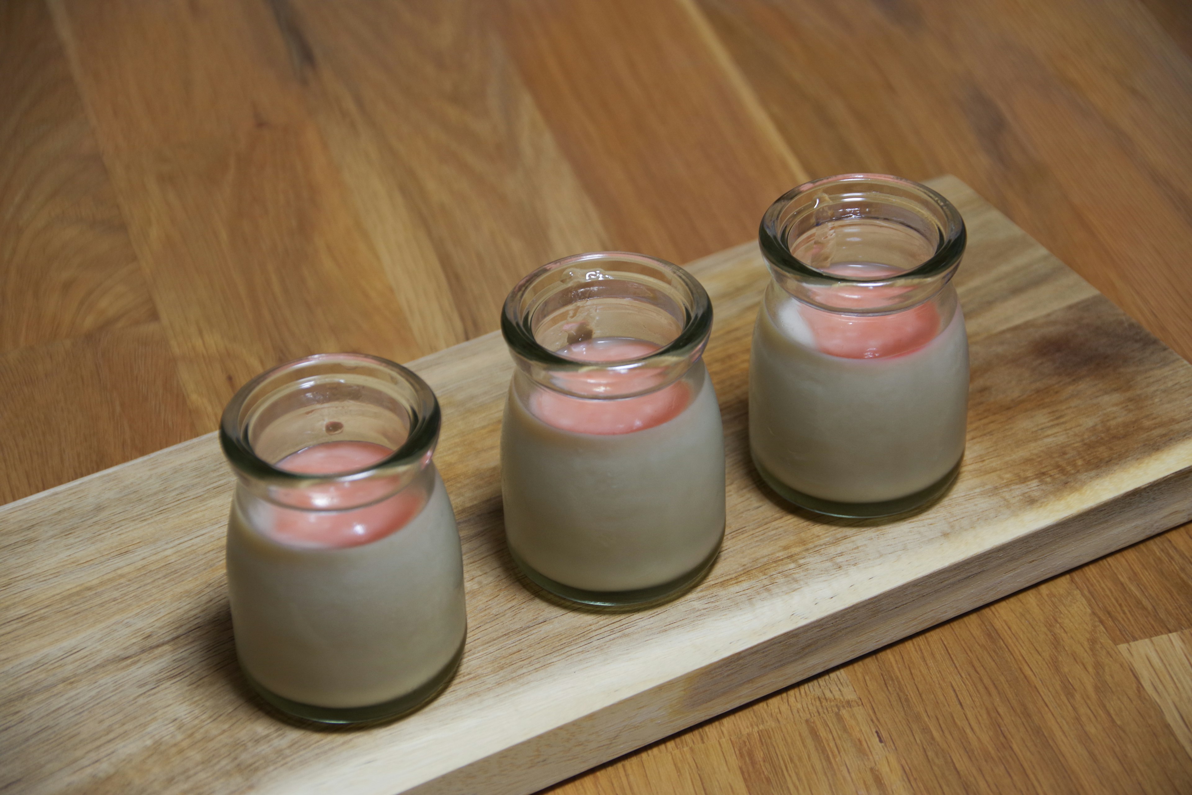 Three glass candle holders with pink candles on a wooden tray