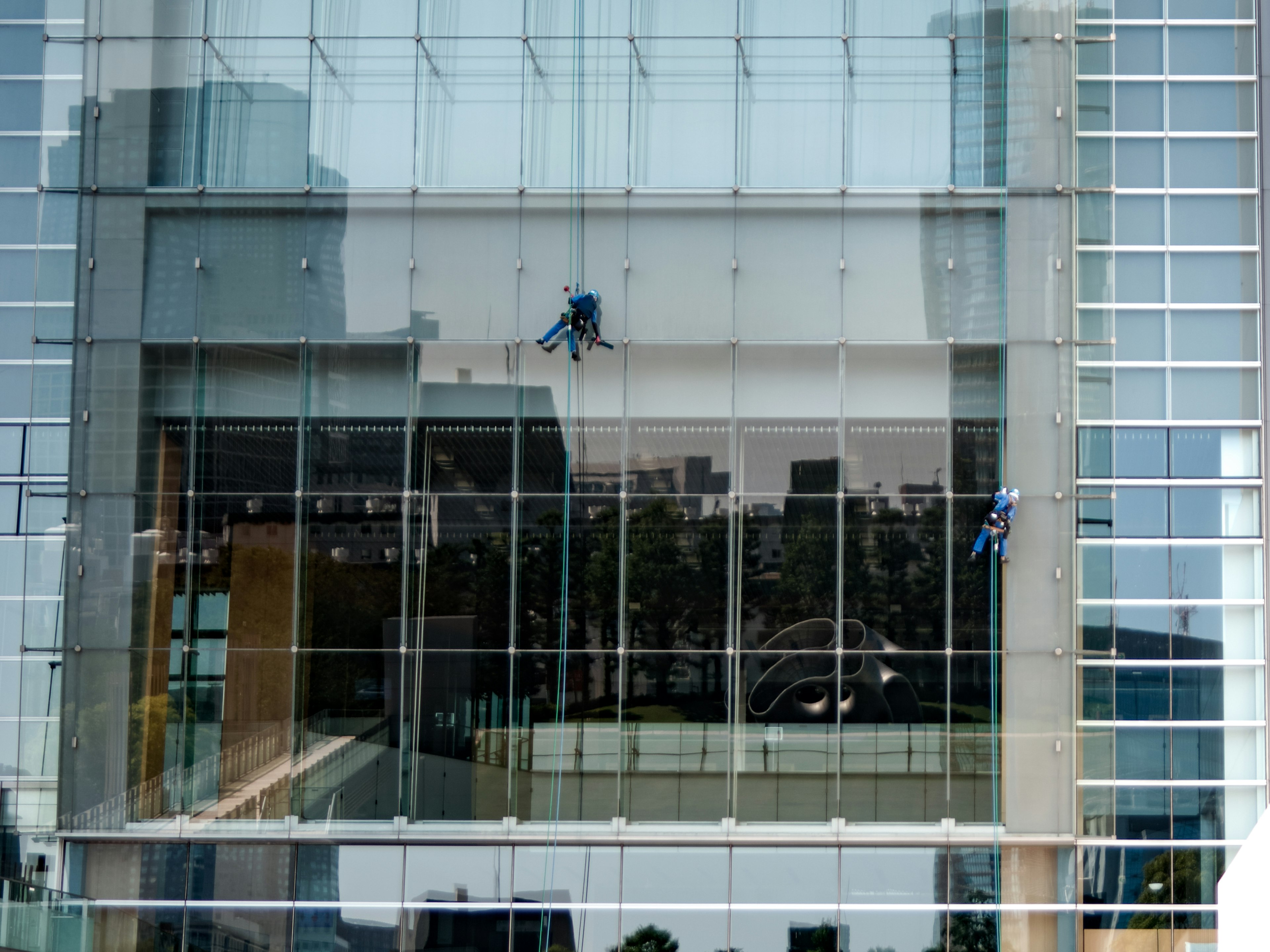 Dua pekerja membersihkan fasad kaca gedung pencakar langit