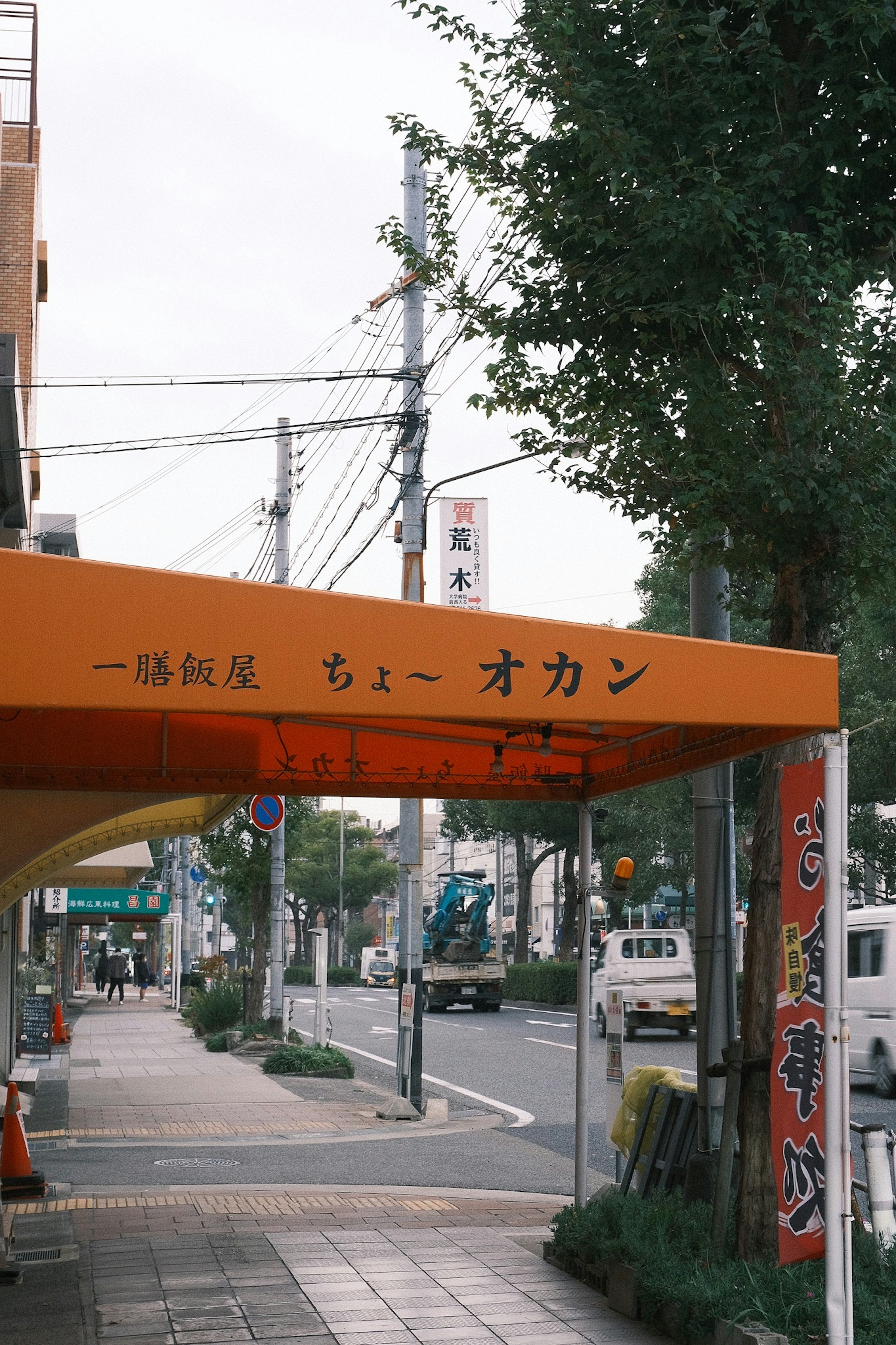 オレンジ色の看板が印象的な通りの風景 店舗の名前は日本語で書かれている