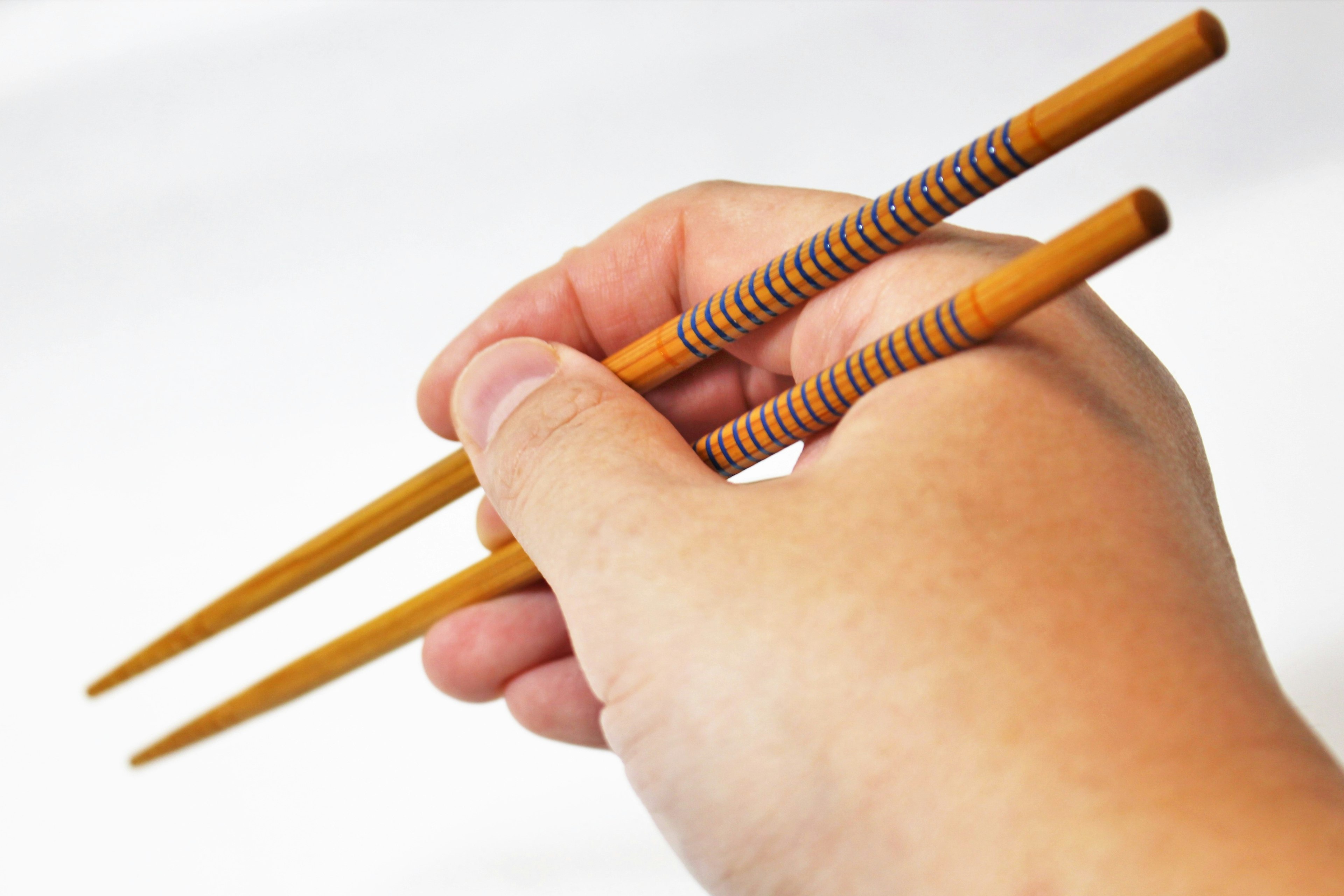 Hand holding wooden chopsticks against a white background