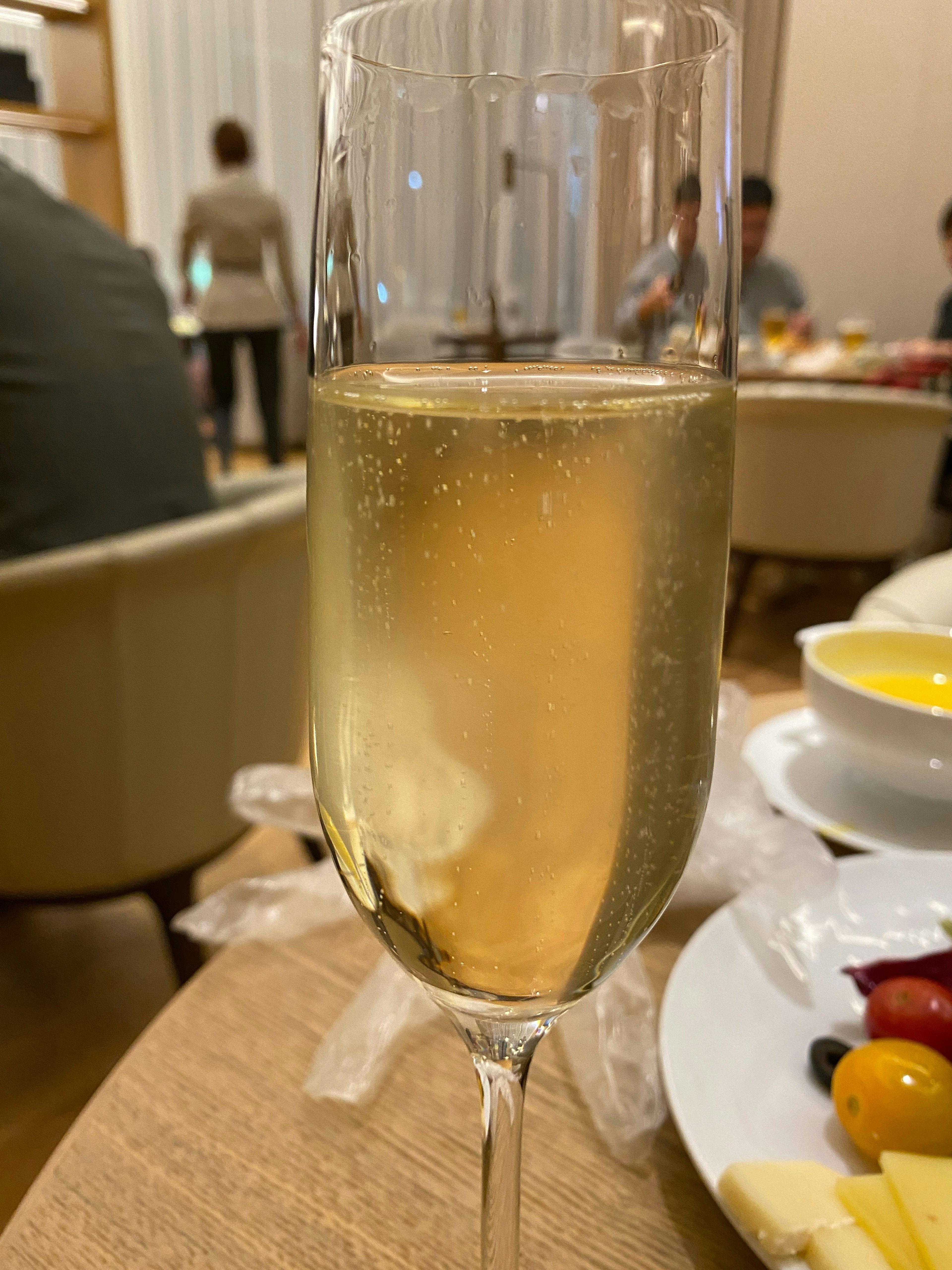 A sparkling beverage in a champagne glass with food in the background