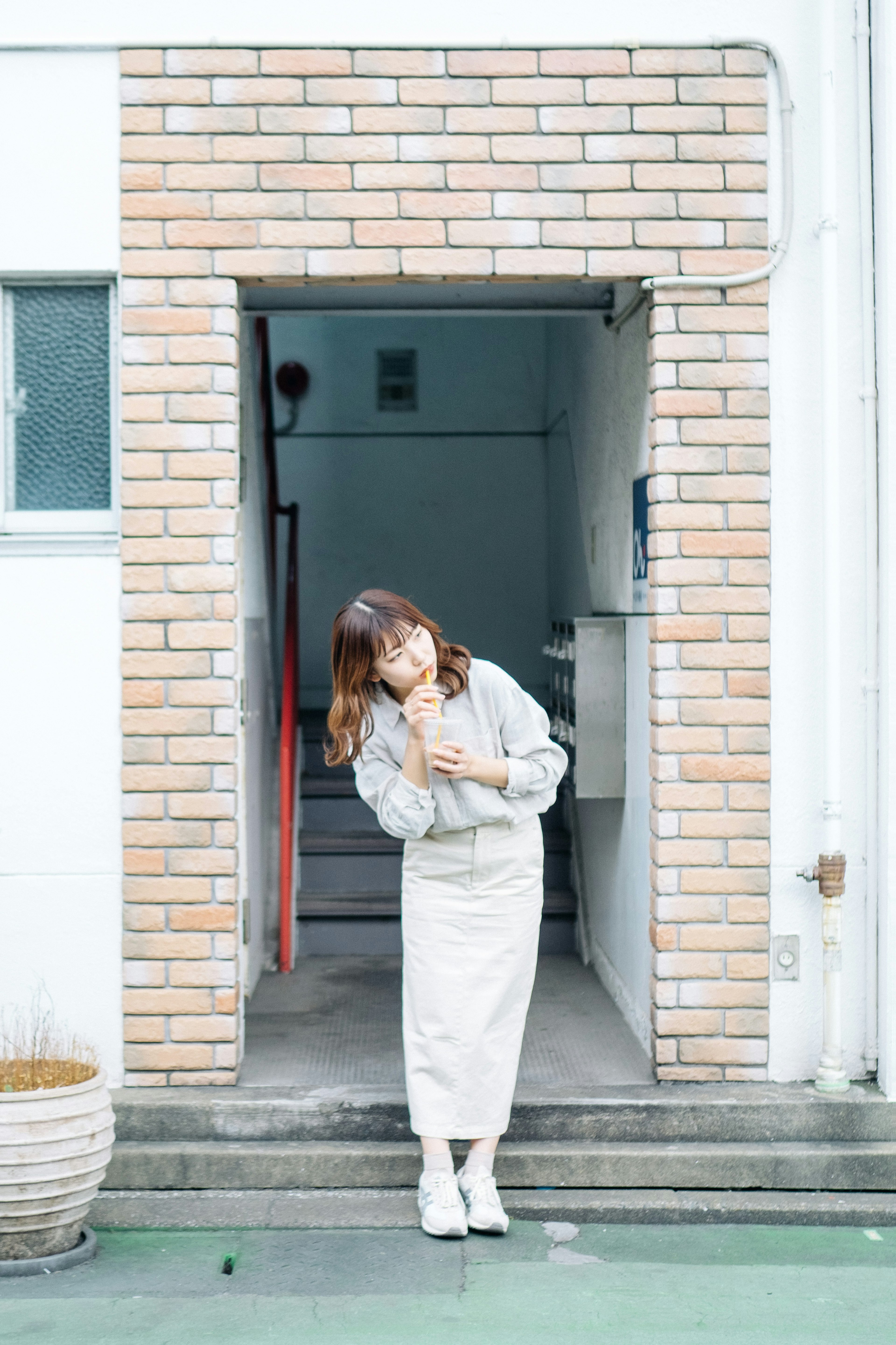 Une femme en jupe blanche et pull posant devant une arche en briques