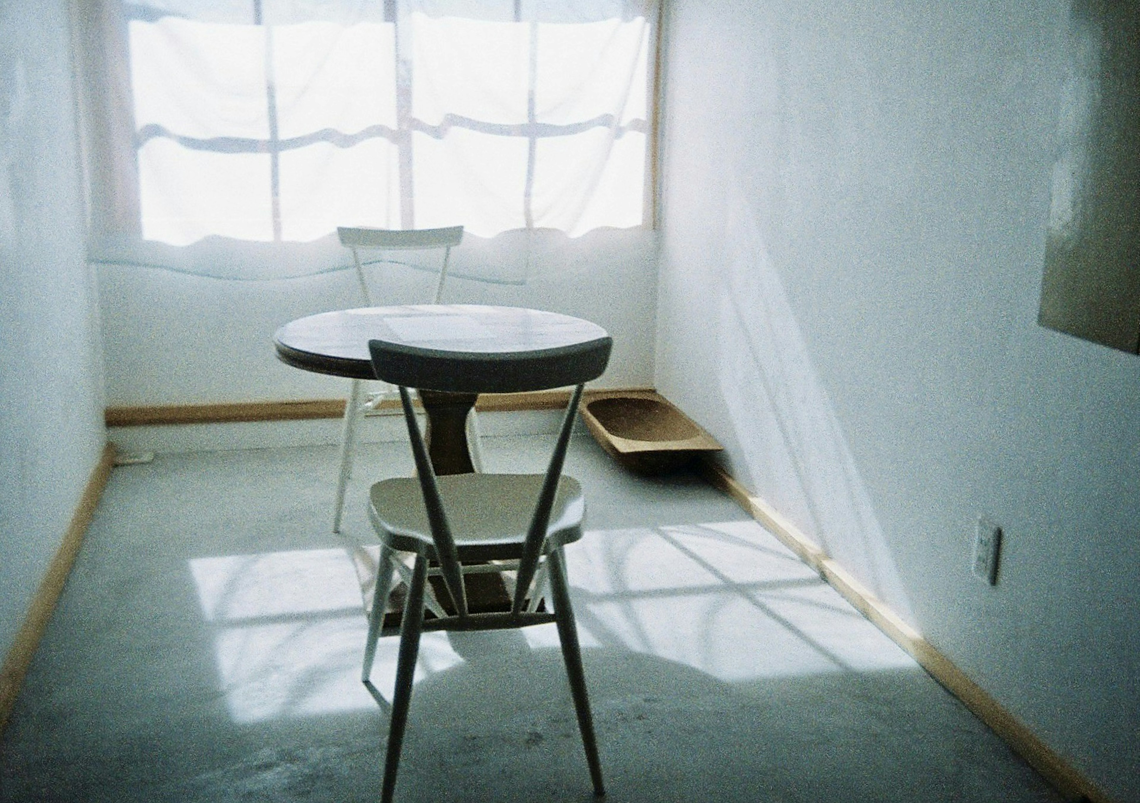 Una habitación simple con paredes blancas, una mesa pequeña y sillas junto a una ventana