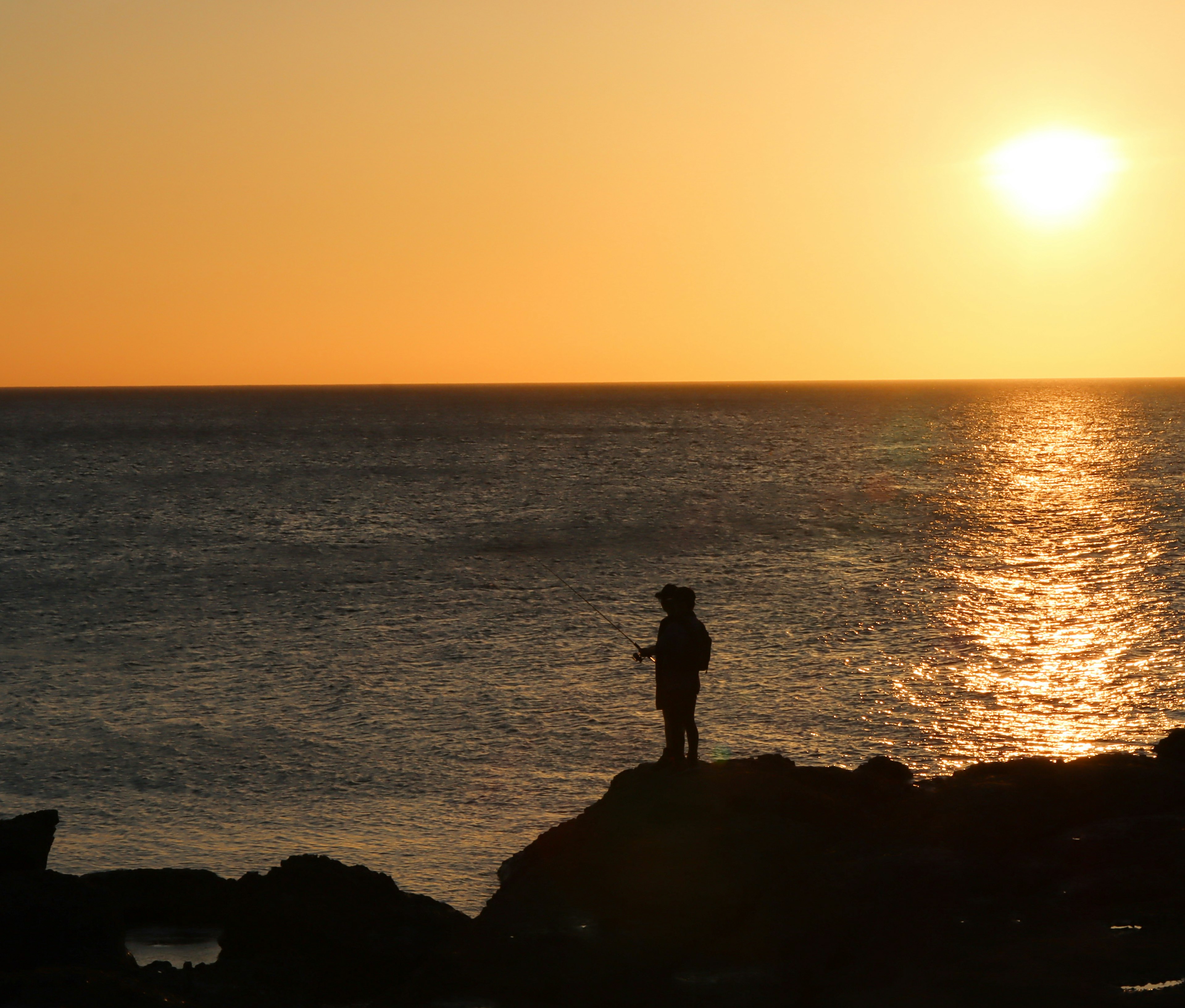 Silhouette of a person standing on rocks by the sea at sunset