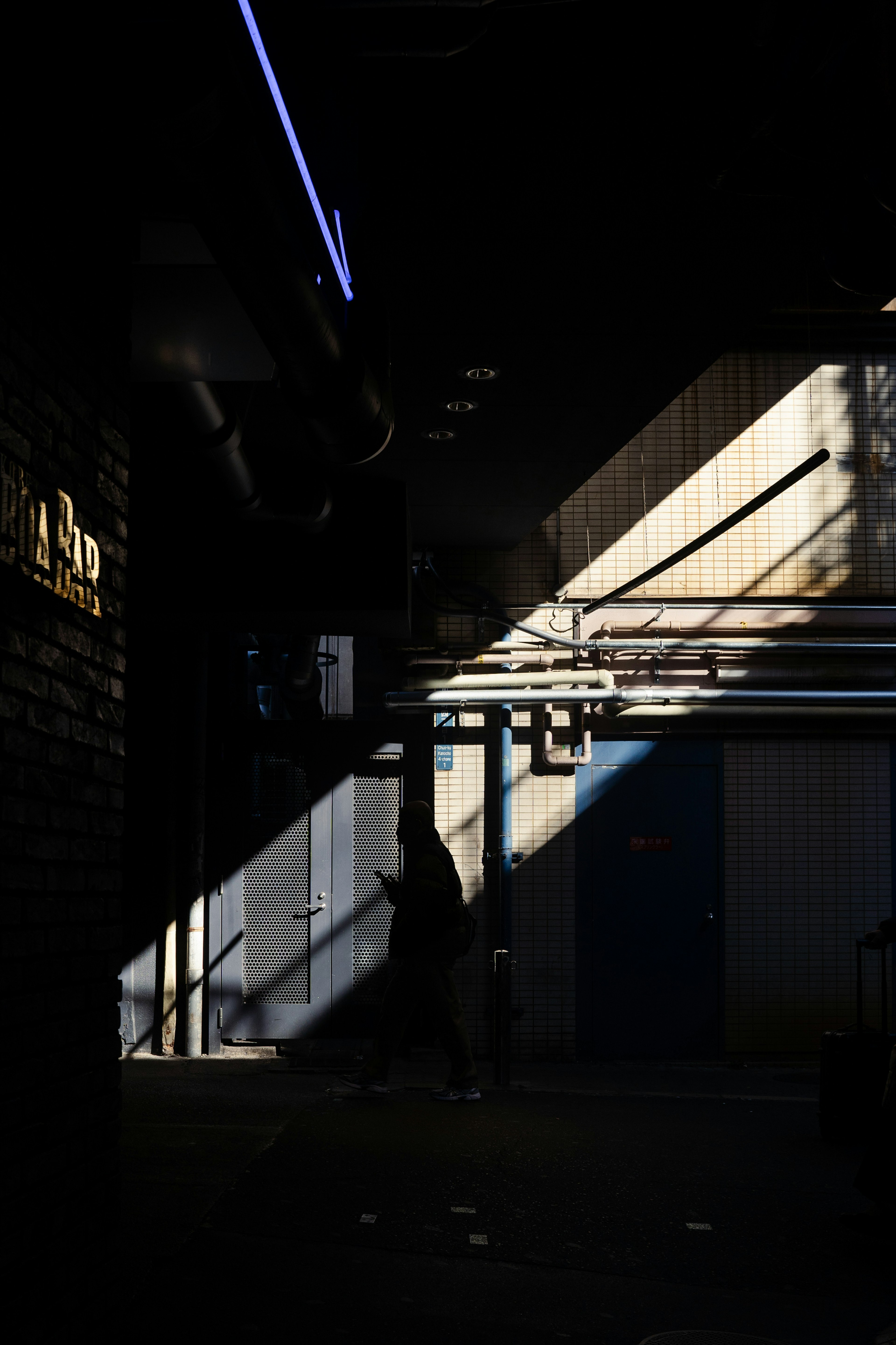 A silhouette of a person walking through a dark corridor with diagonal light beams