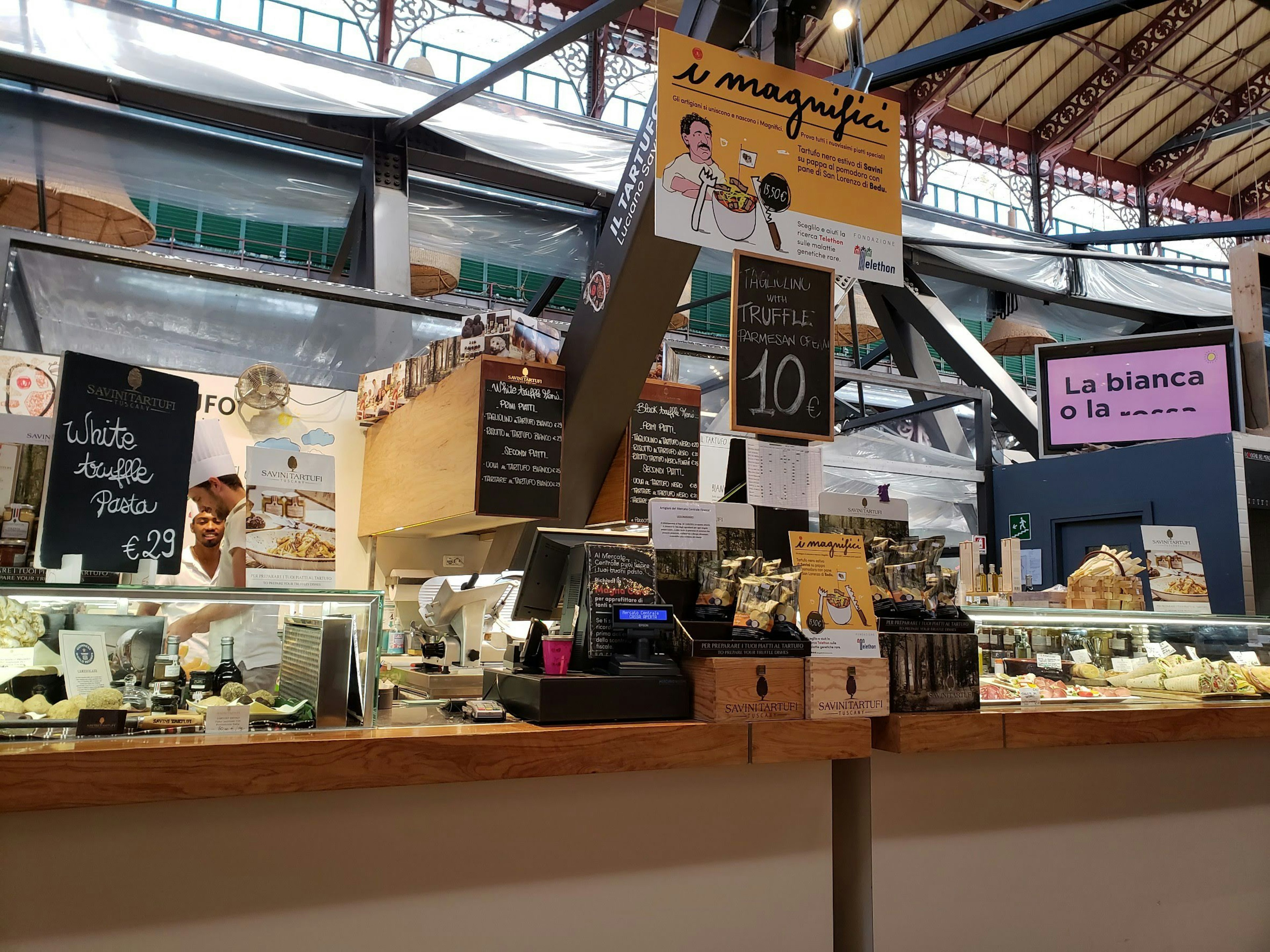 Cheese shop counter in a market displaying various cheeses and signage