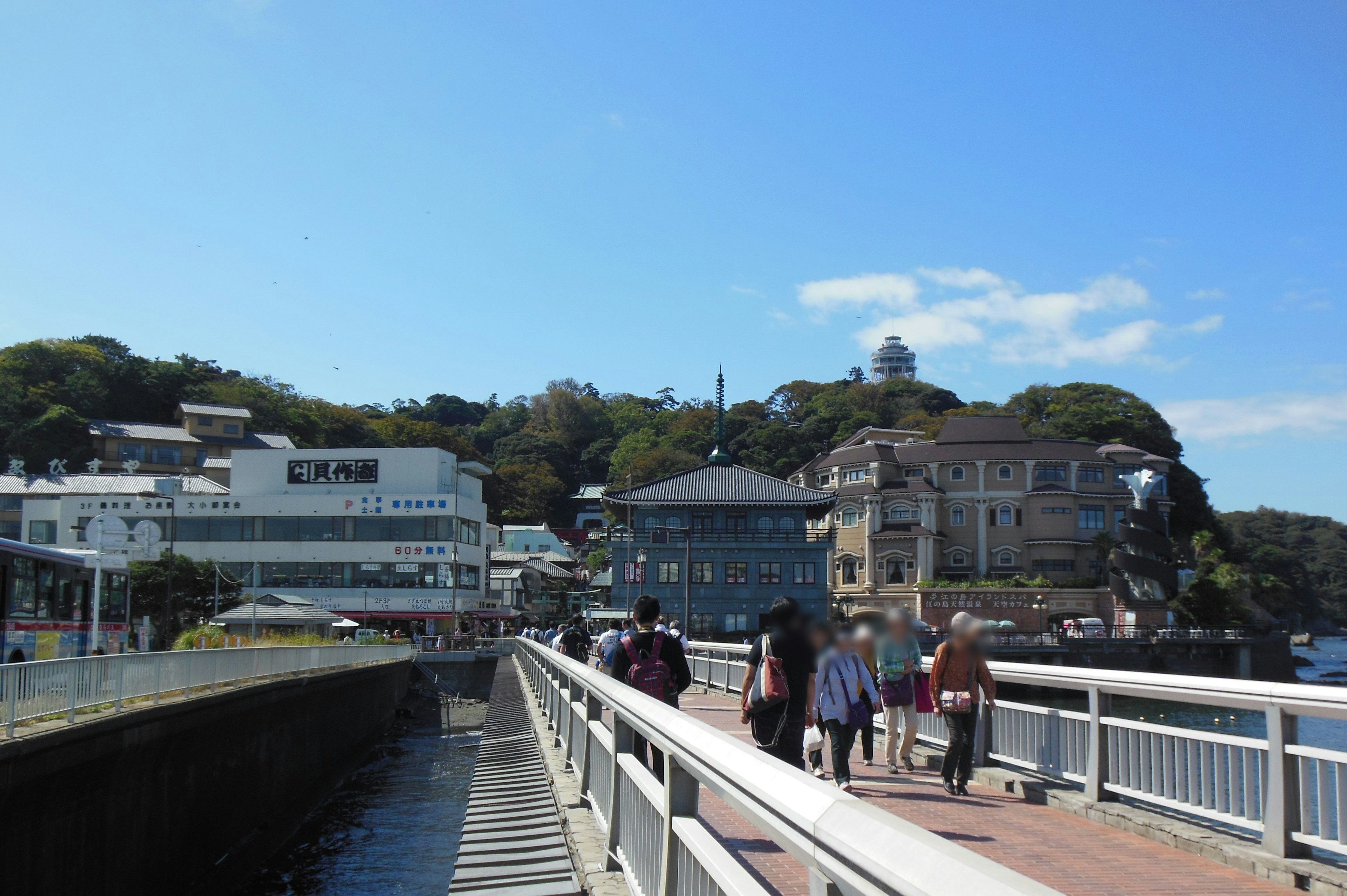 海沿いの遊歩道に人々が歩いている風景青い空と緑の丘が背景