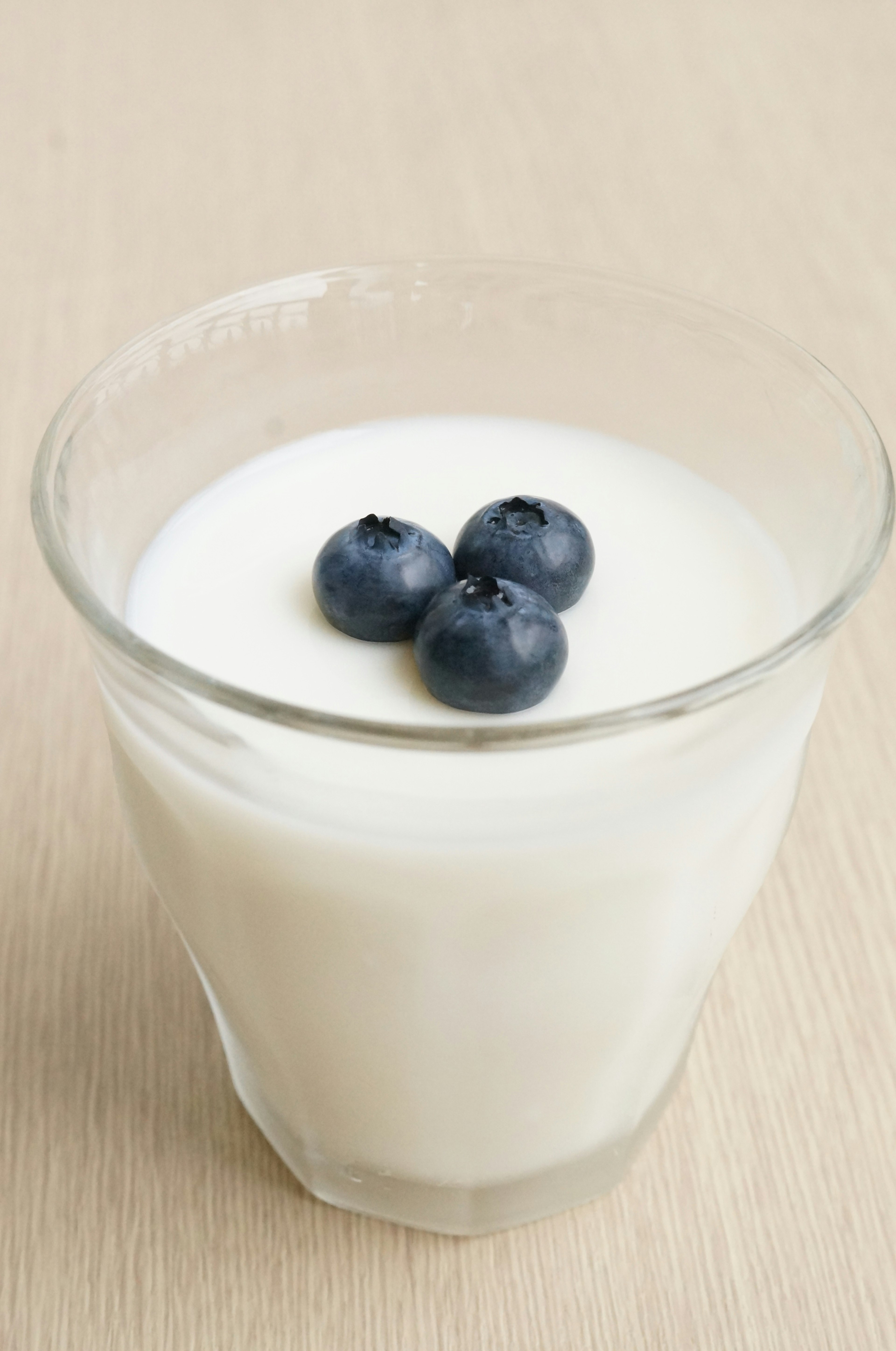 A clear glass containing yogurt topped with three blueberries