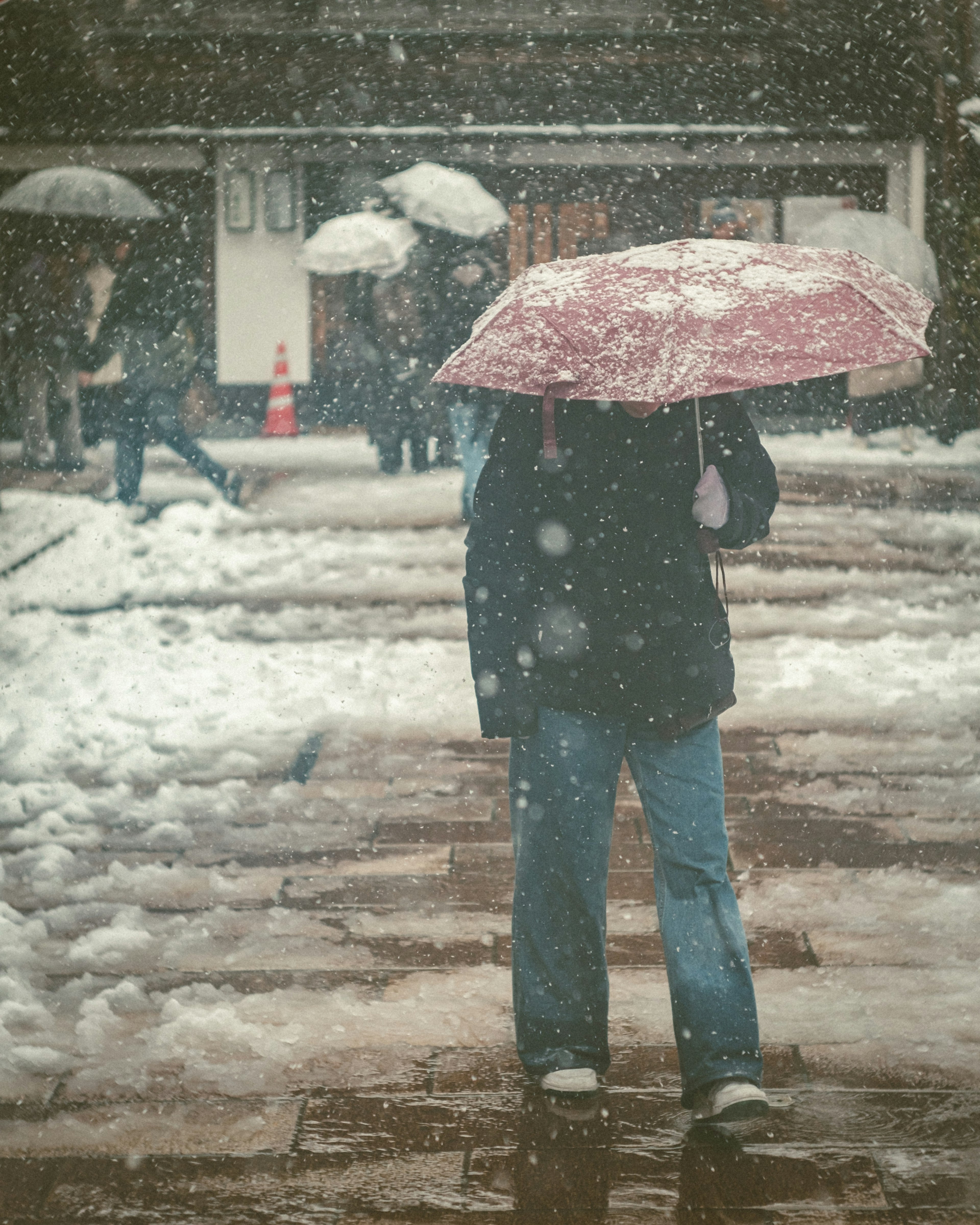 在雪中撑着红伞的人周围是被雪覆盖的街道和其他撑伞的人