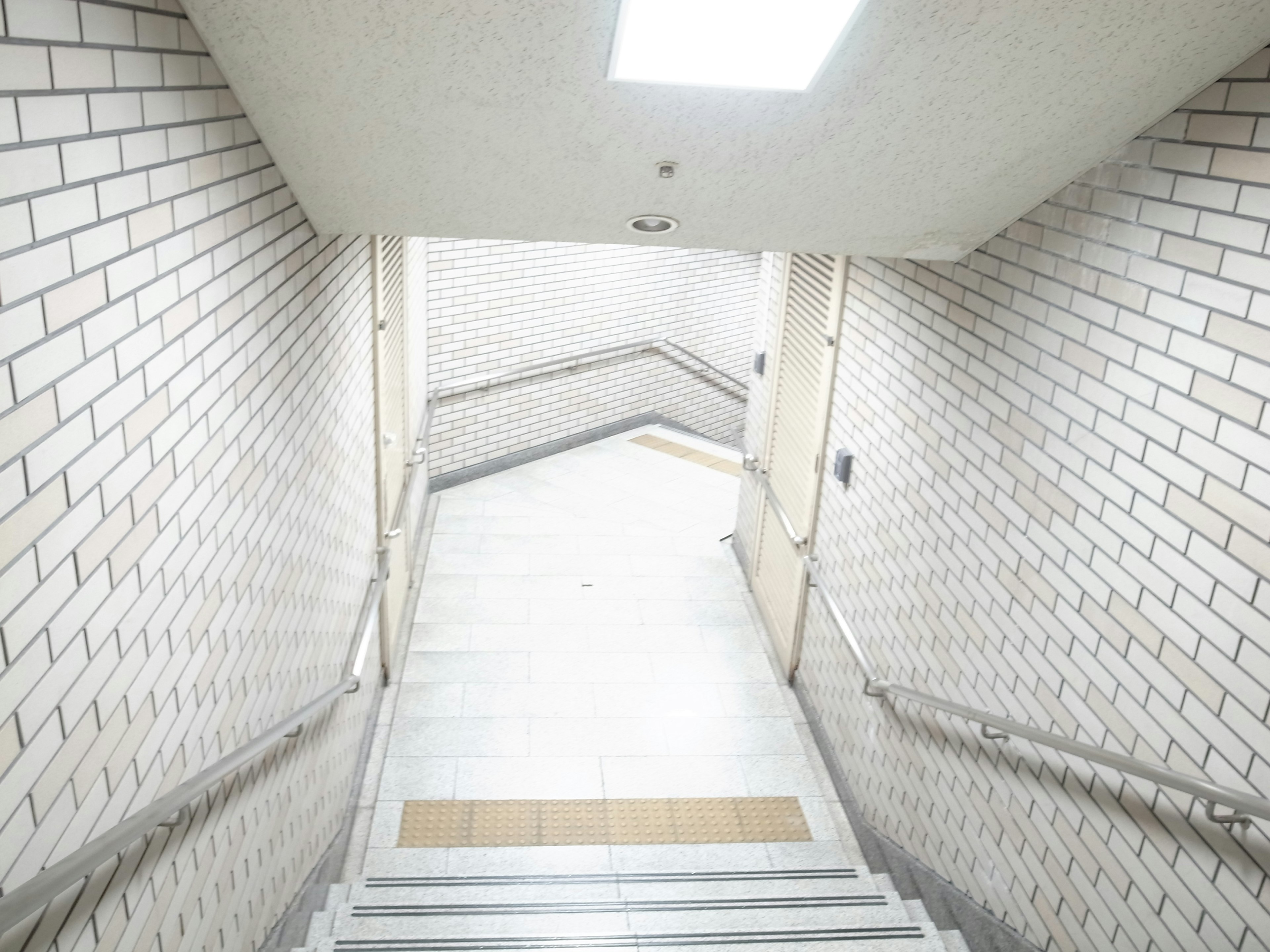 Escalera con azulejos blancos y paredes de ladrillo en un pasillo de sótano