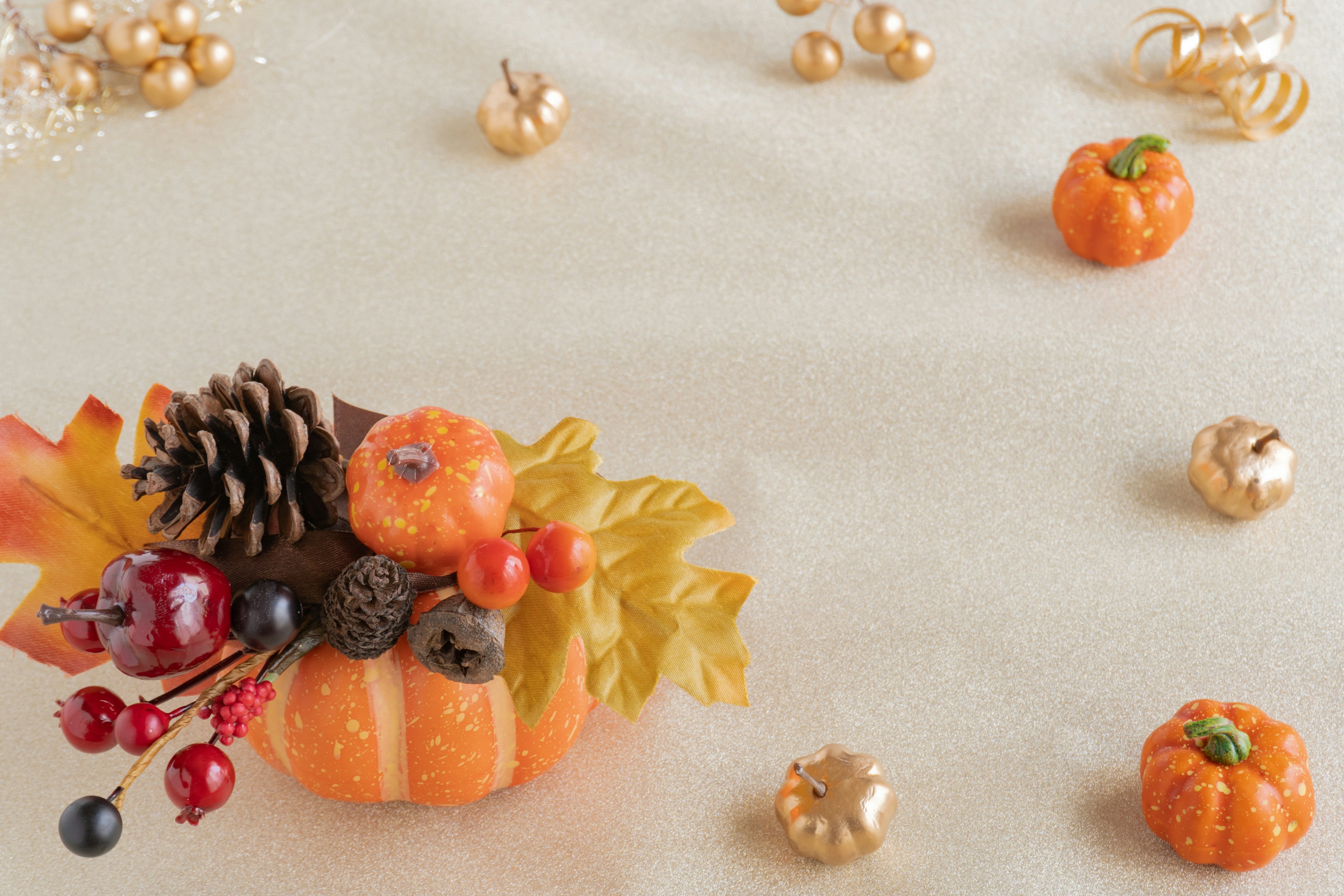 Autumn arrangement featuring orange mini pumpkins and pine cones with gold decorations