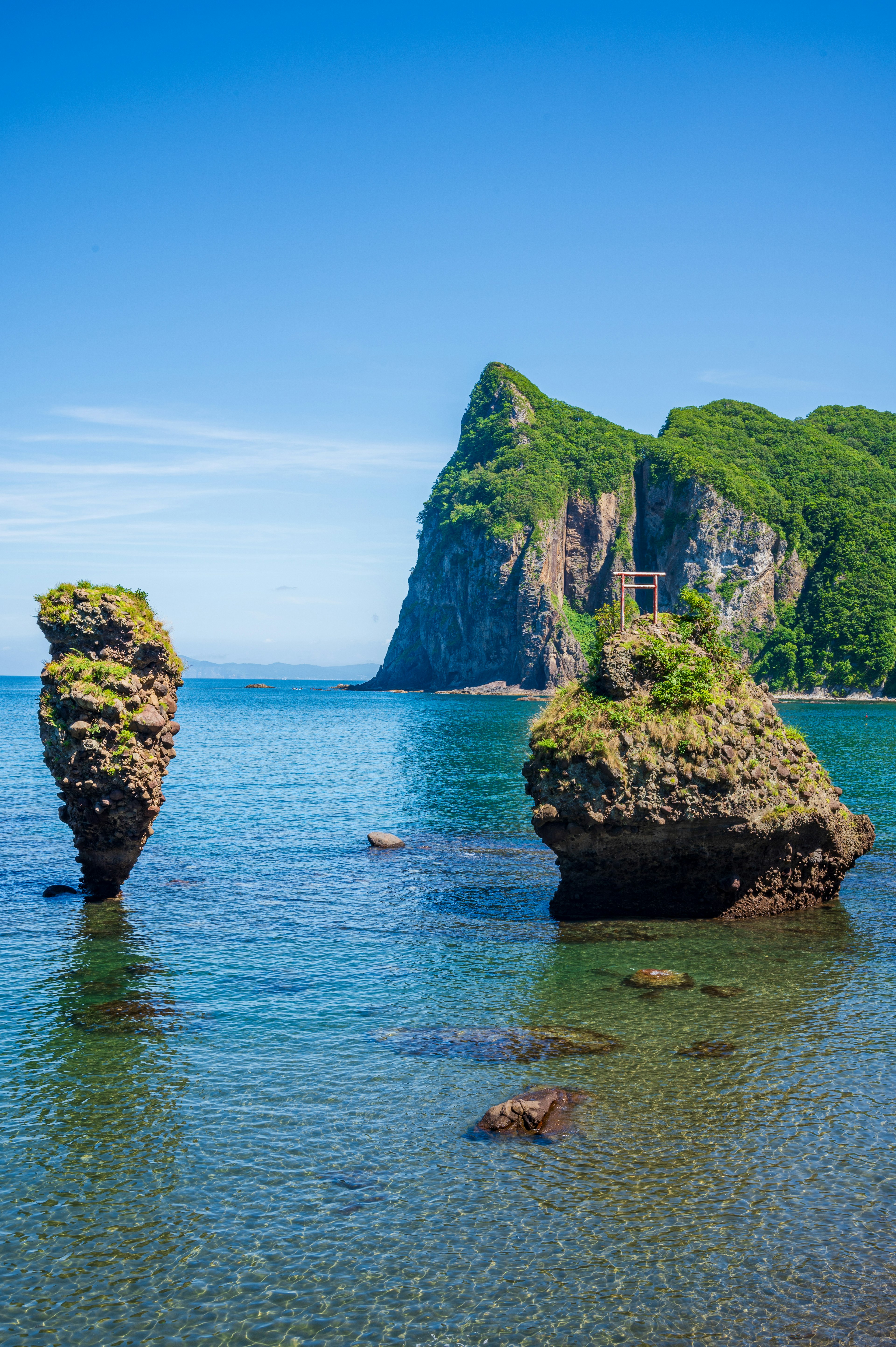 Scenic view of two rock formations with a torii gate surrounded by blue sea and green mountains