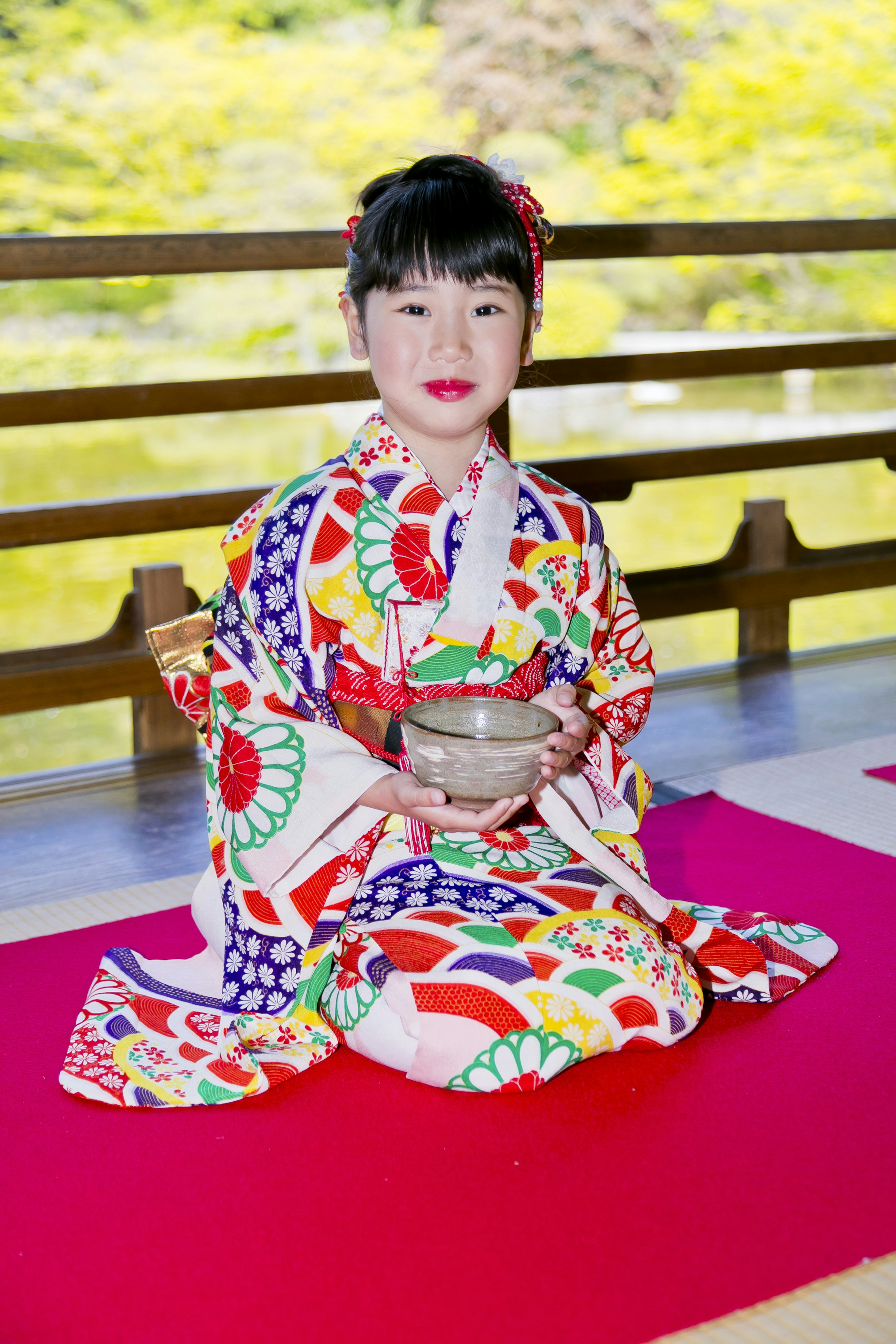 Una niña en un kimono colorido sosteniendo un tazón de té mientras está sentada