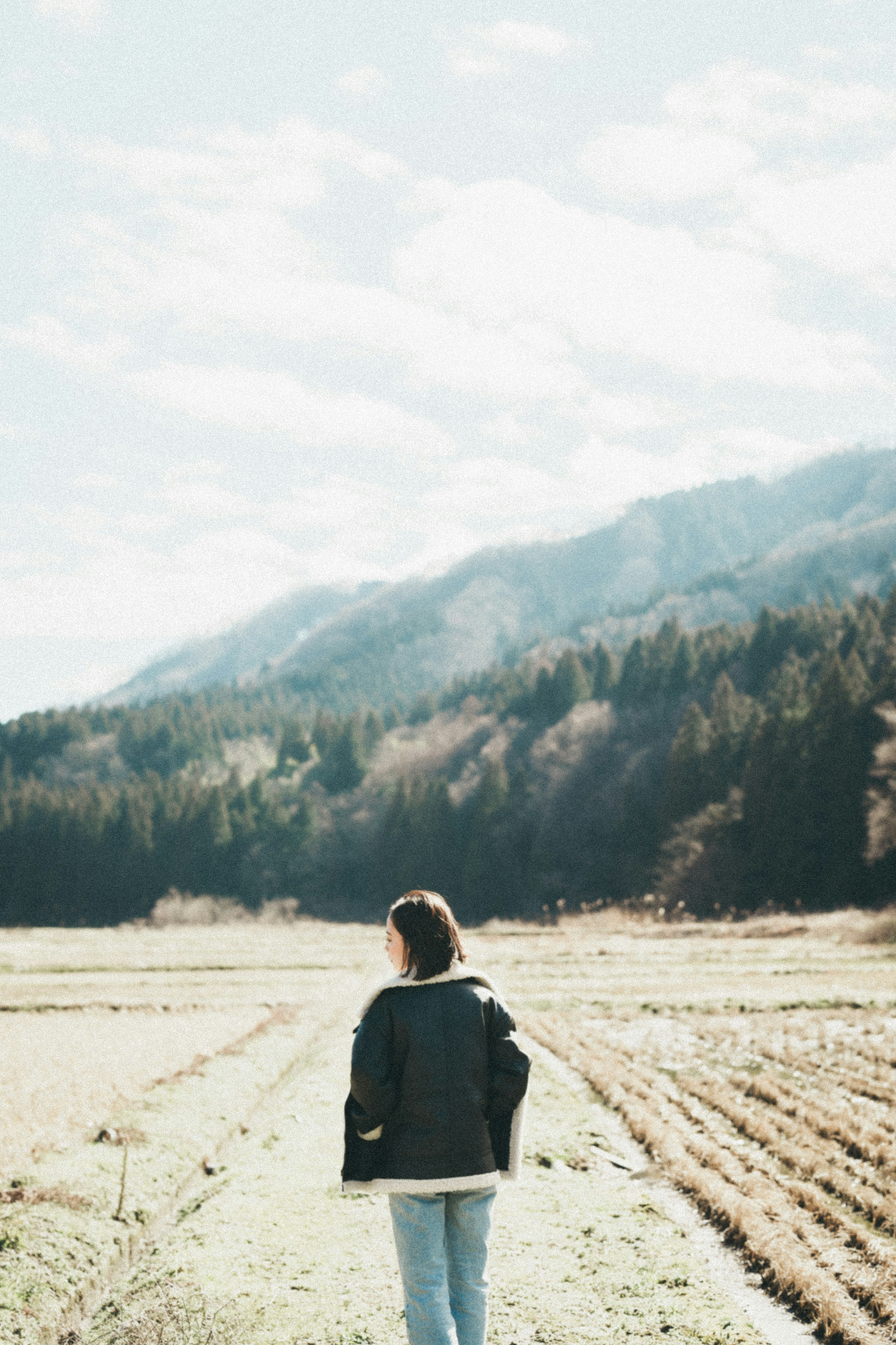 A young woman walking in a wide field with mountains in the background