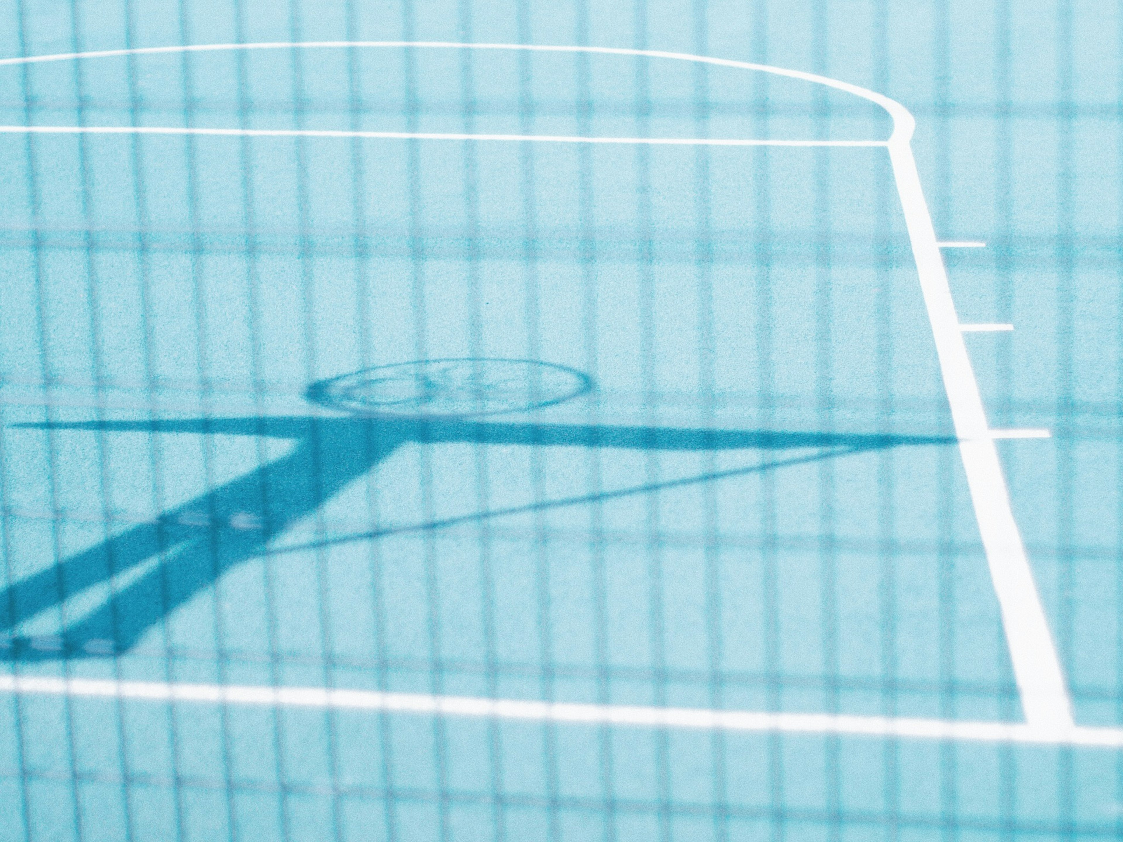 Part of a blue basketball court with shadow seen through the net