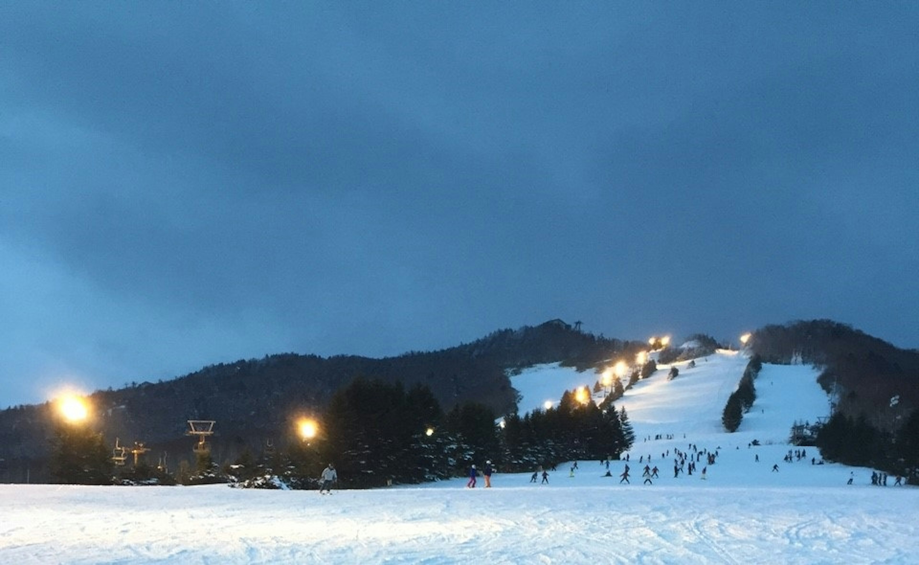 Vista notturna di una stazione sciistica innevata con sciatori sulle piste e colline illuminate