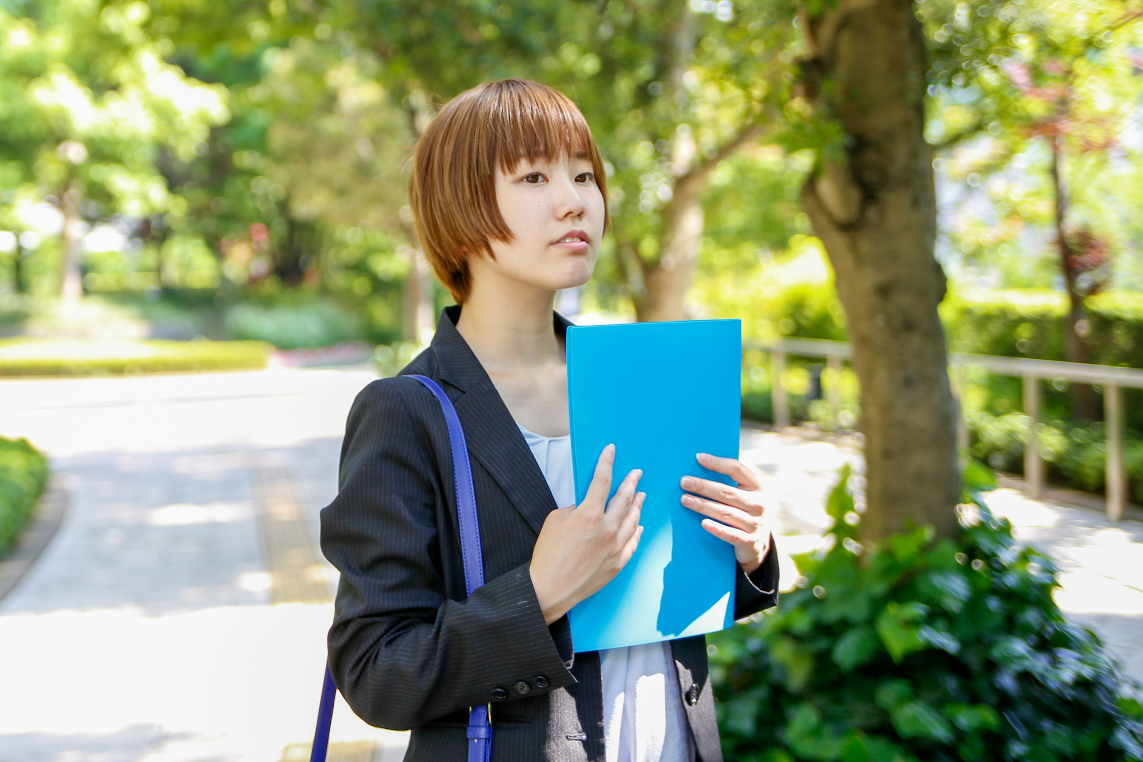 Woman holding a blue folder in a park looking thoughtful