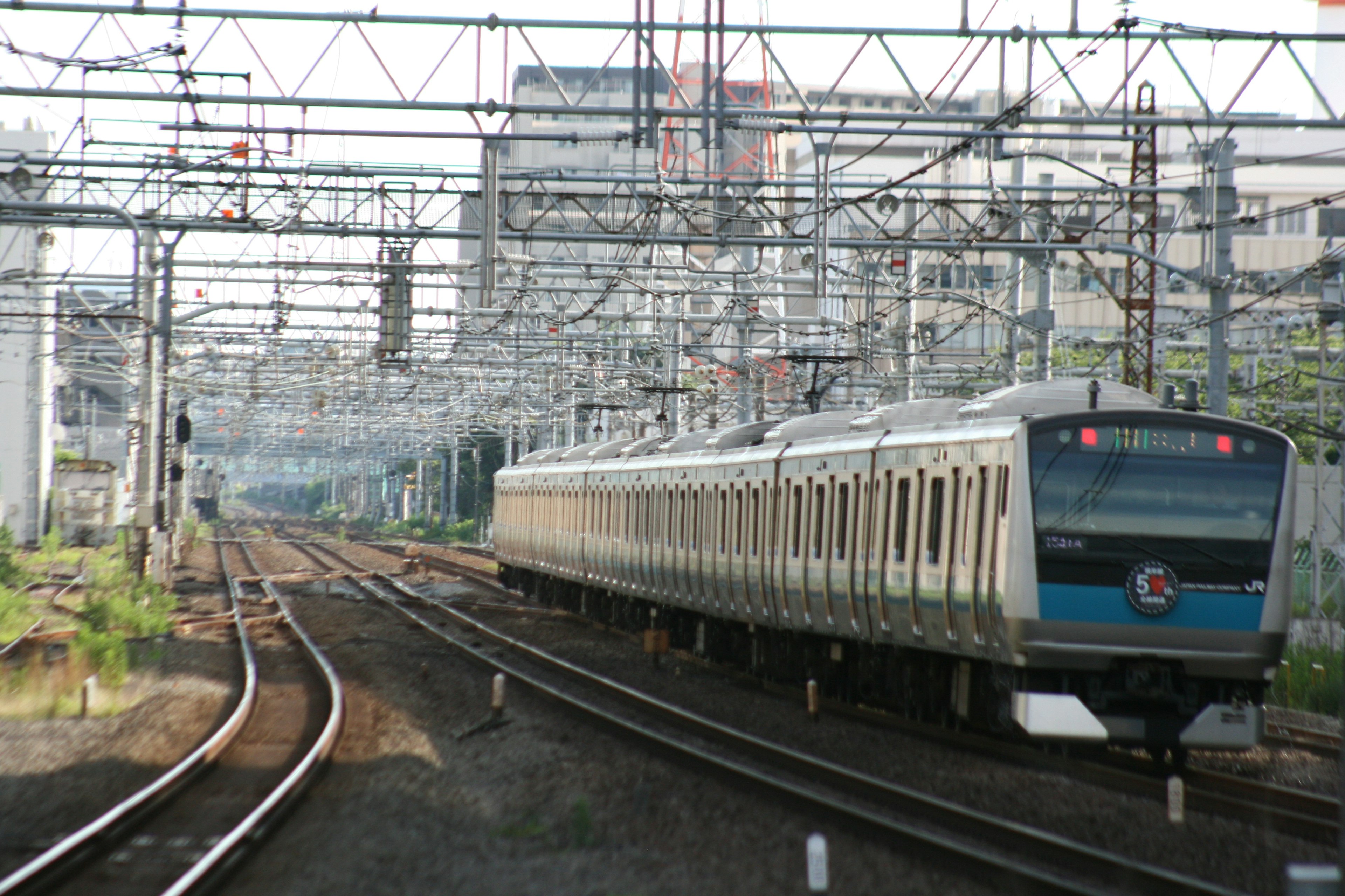 Train traveling on tracks surrounded by overhead wires and urban buildings