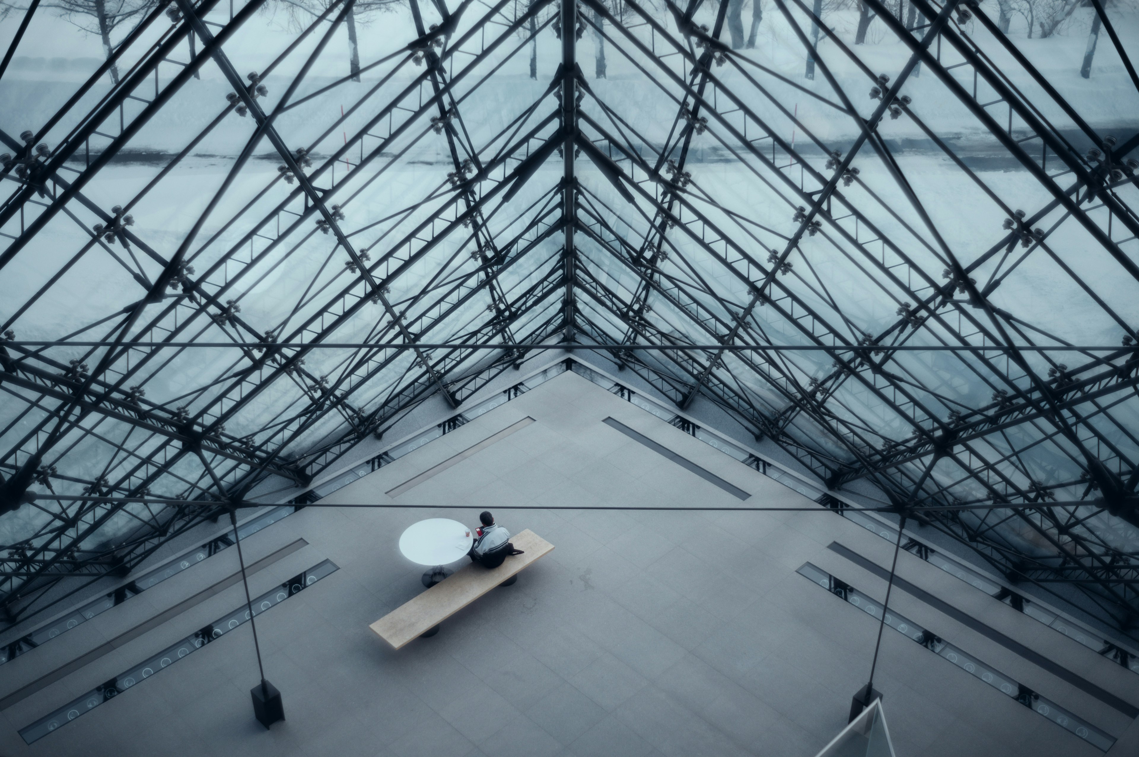 Interno della piramide del Louvre che mostra la sua struttura in vetro e un tavolo semplice