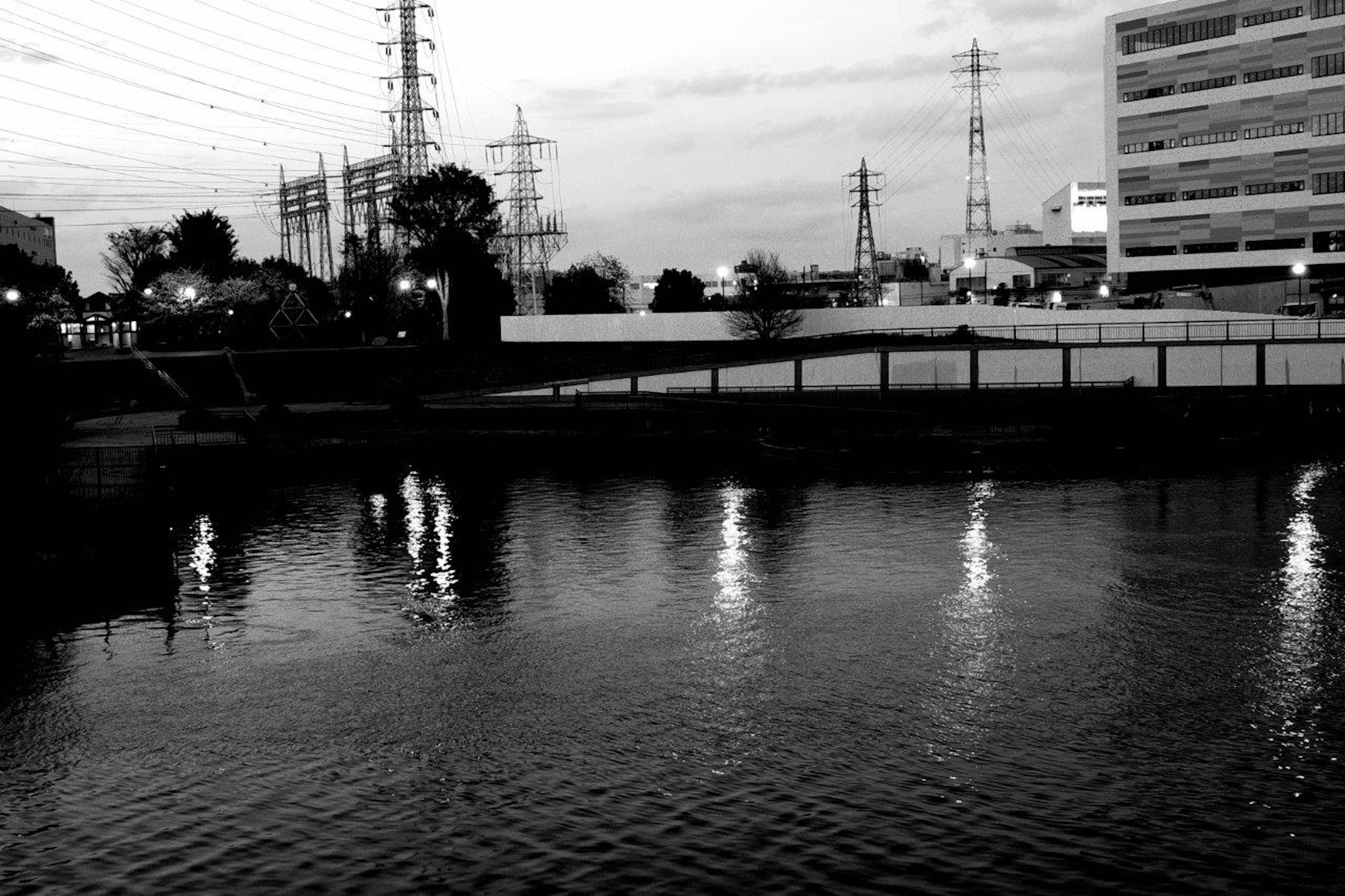 Imagen en blanco y negro de un río reflejando las luces de la ciudad y líneas de energía