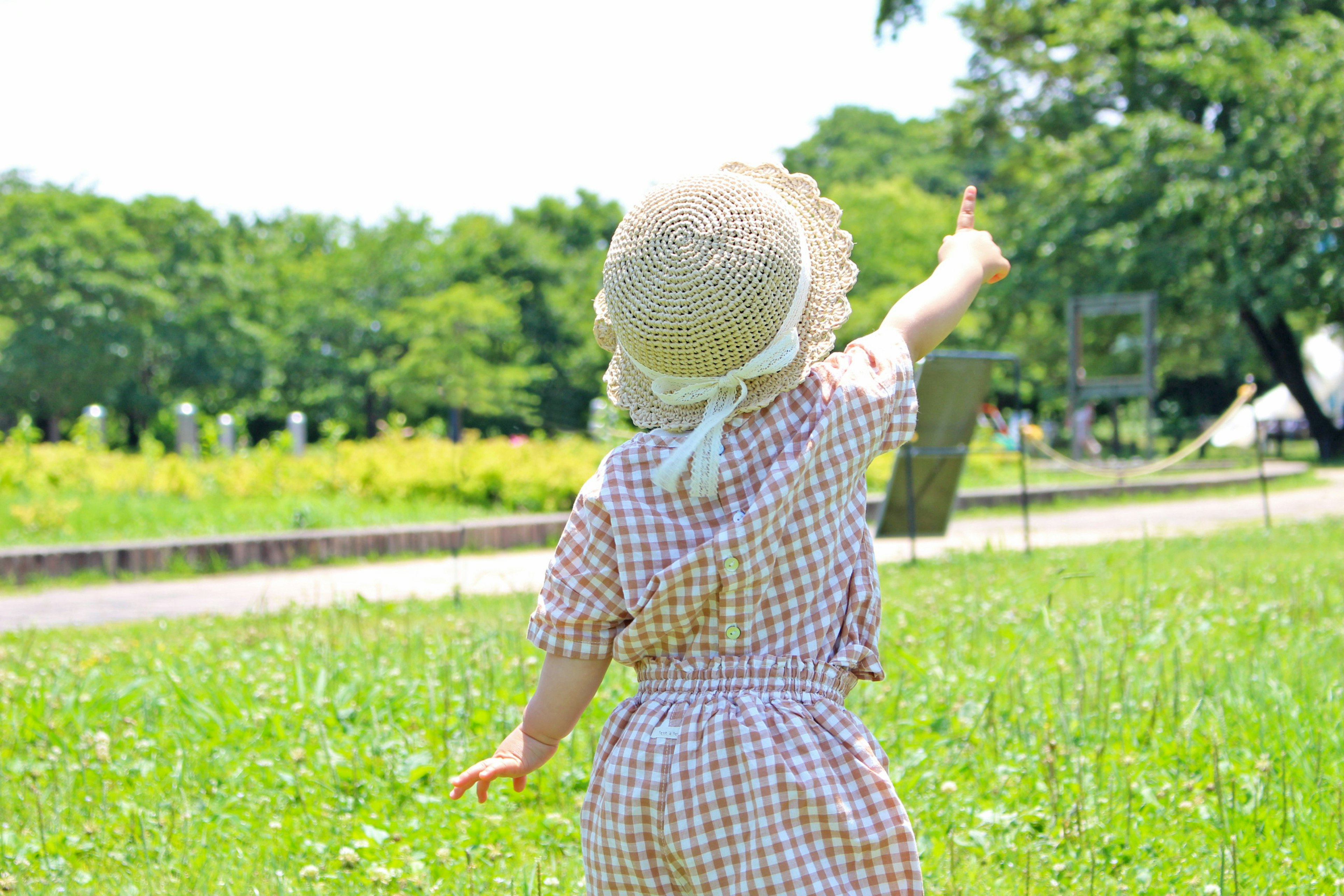 一個孩子在公園裡指著天空 背景是綠色的草坪和樹木