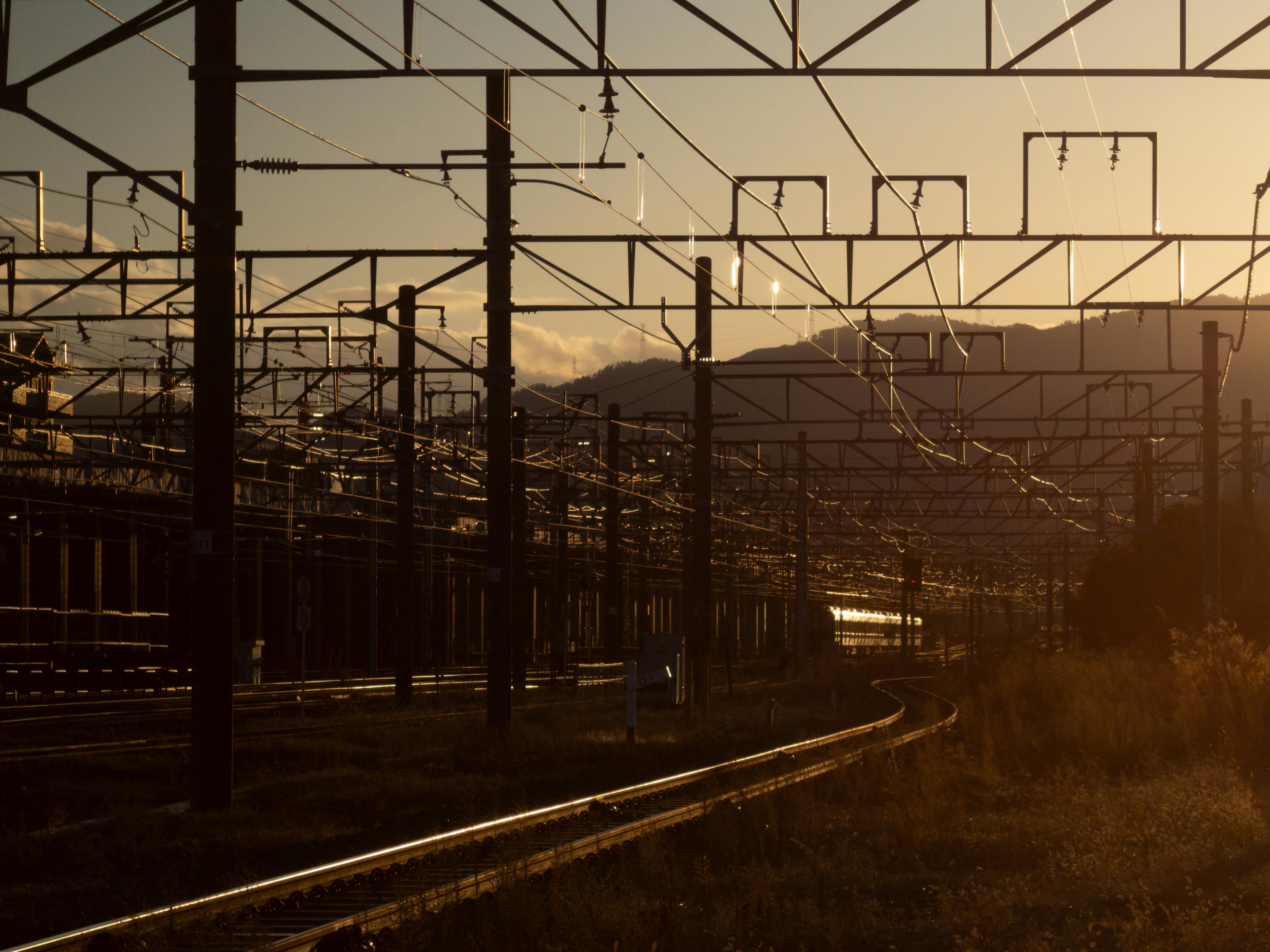 Scenic view of railway tracks with silhouetted mountains at sunset