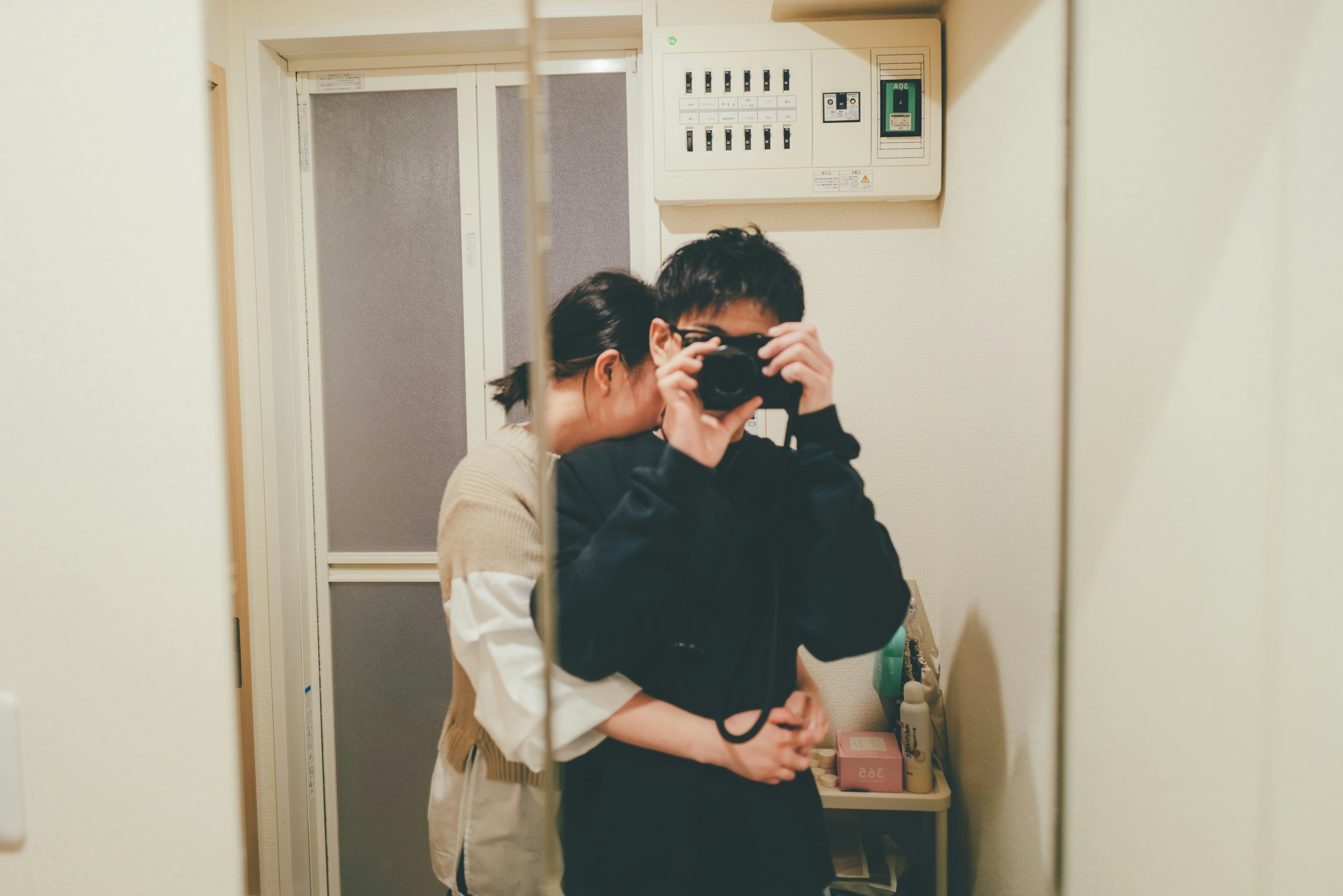 Two people embracing while taking a selfie in front of a mirror