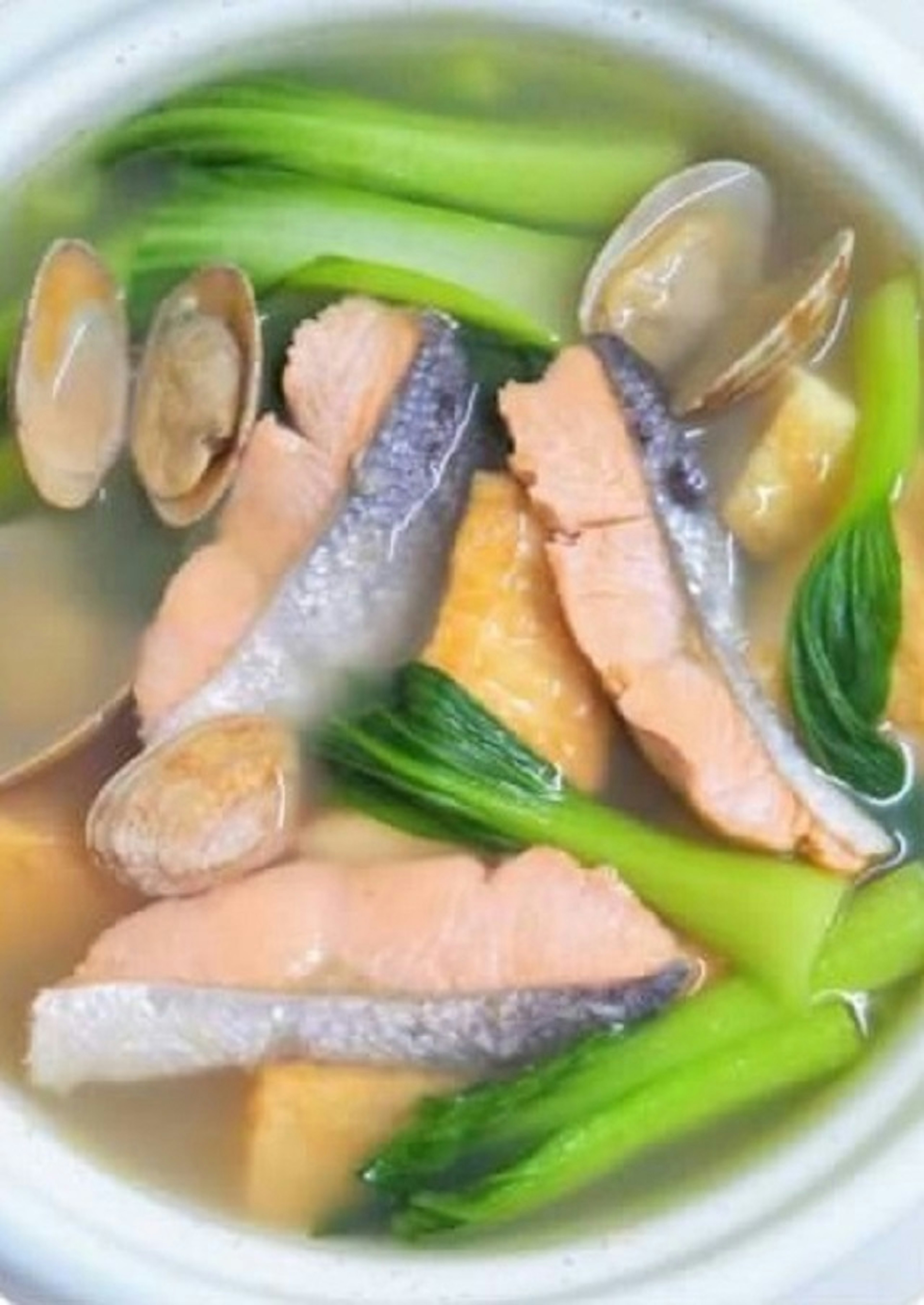 A vibrant soup featuring sliced salmon, clams, and green vegetables