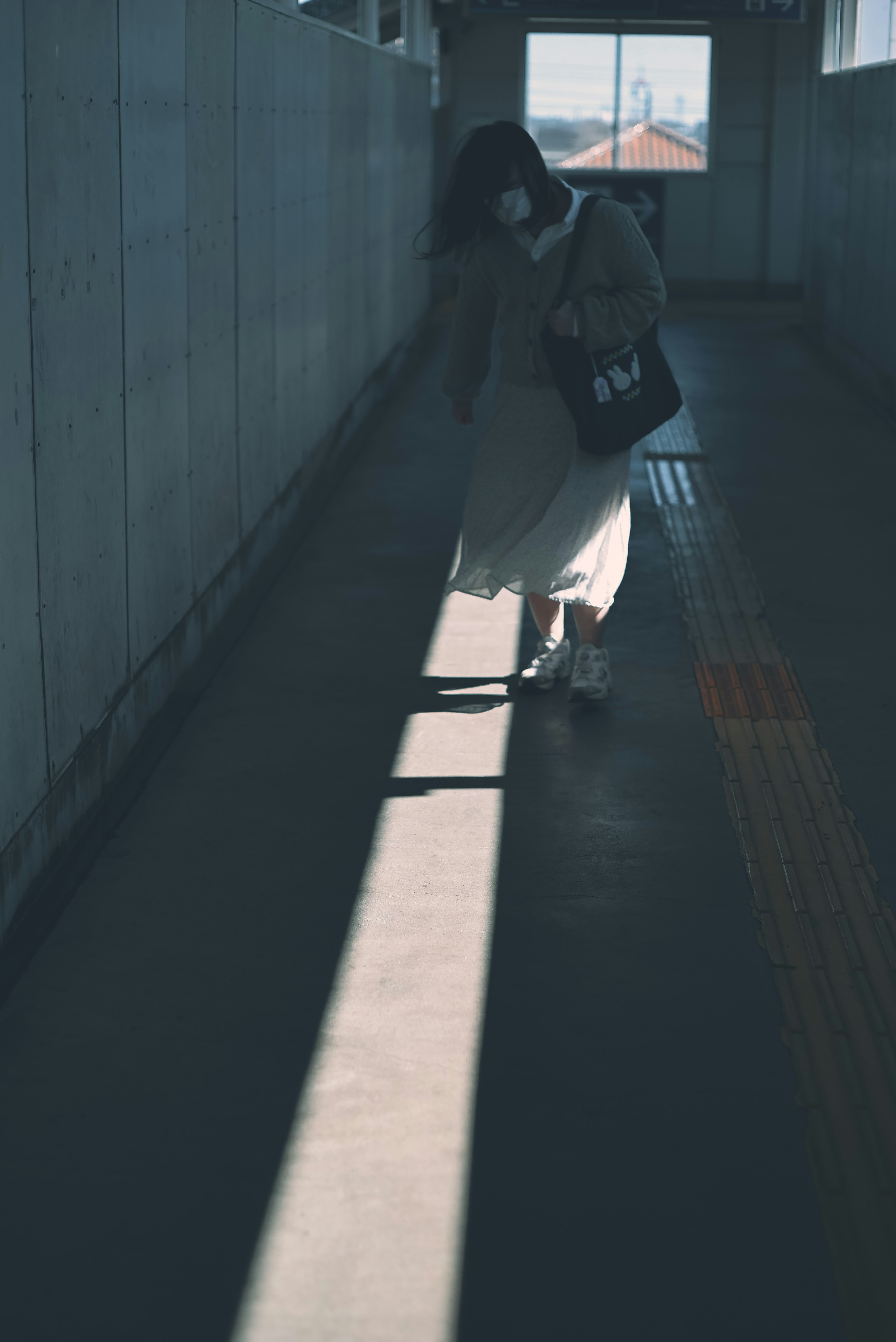 Femme marchant dans une lumière tamisée vêtue d'une robe blanche et portant un sac noir dans un couloir