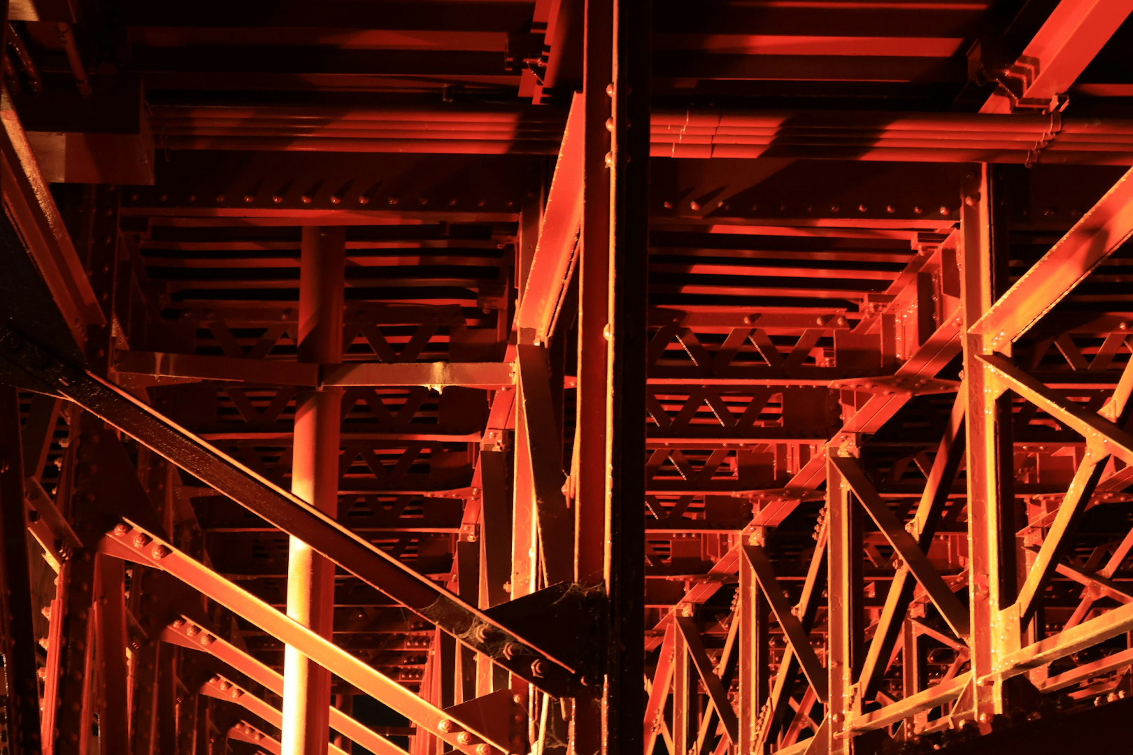 Debajo de un puente con iluminación roja que ilumina la estructura de acero