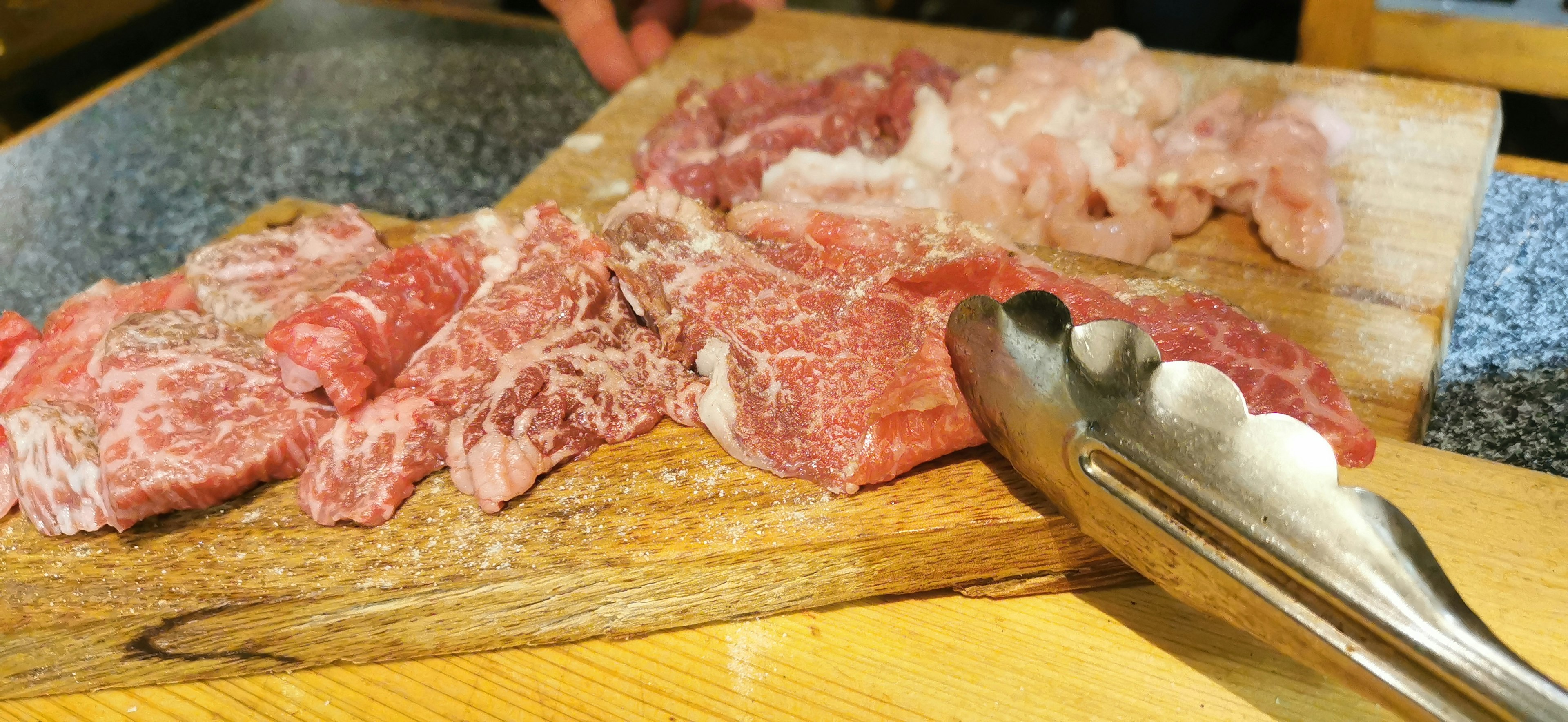 Cortes de carne variados en una tabla de madera con pinzas al lado