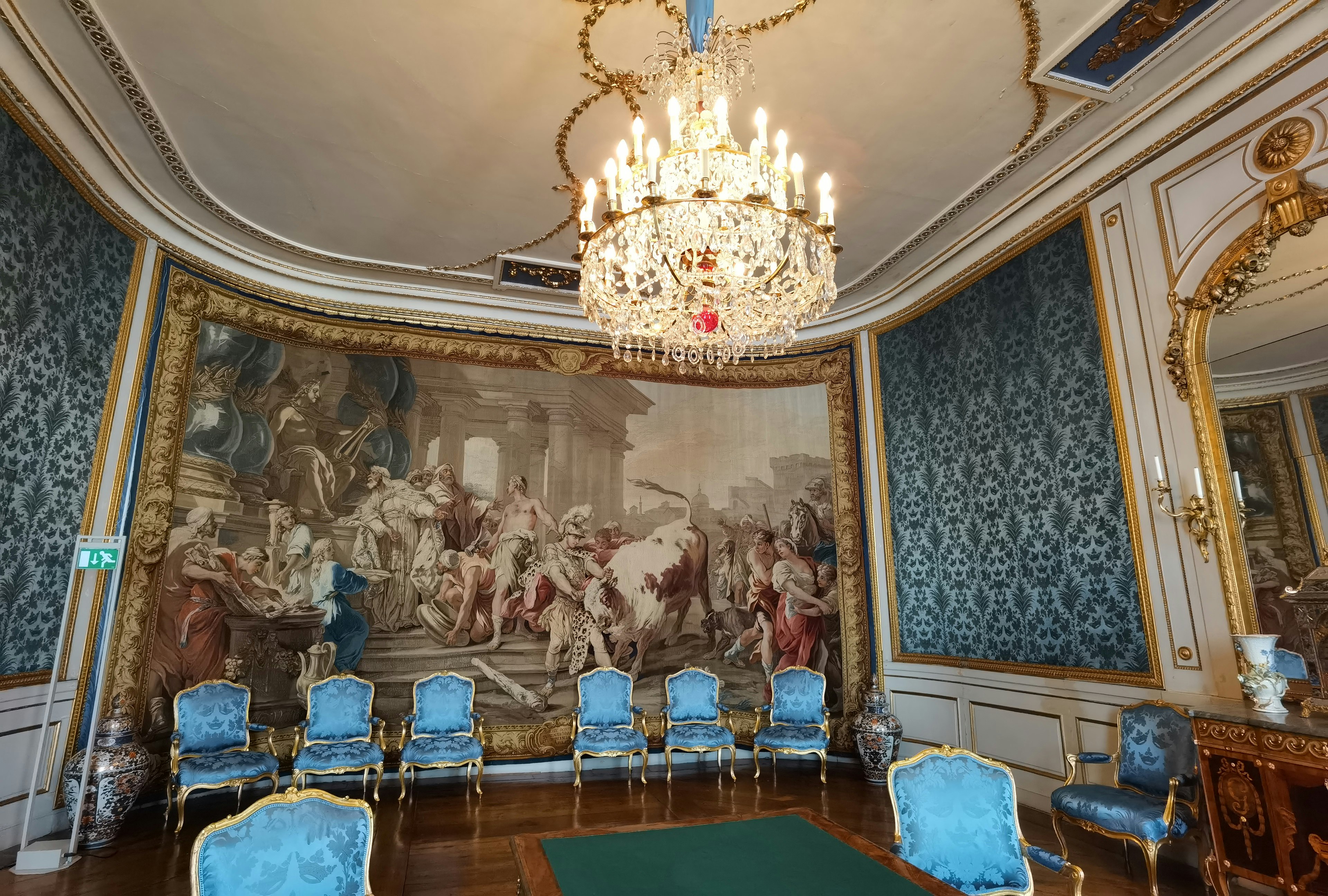 Elegant room featuring a grand chandelier and blue chairs with a stunning fresco on the wall