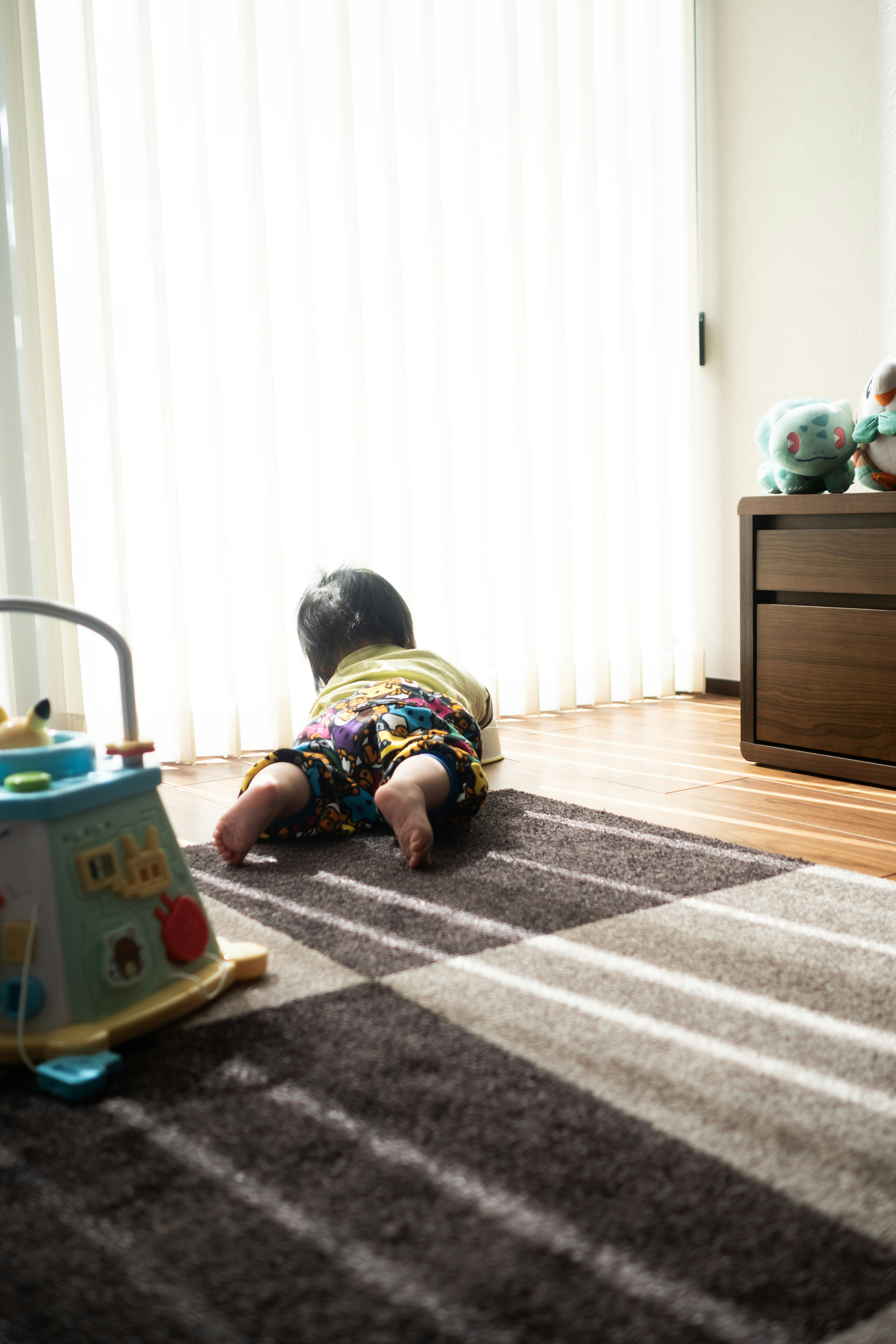 A child in colorful clothing crawling in front of curtains indoors