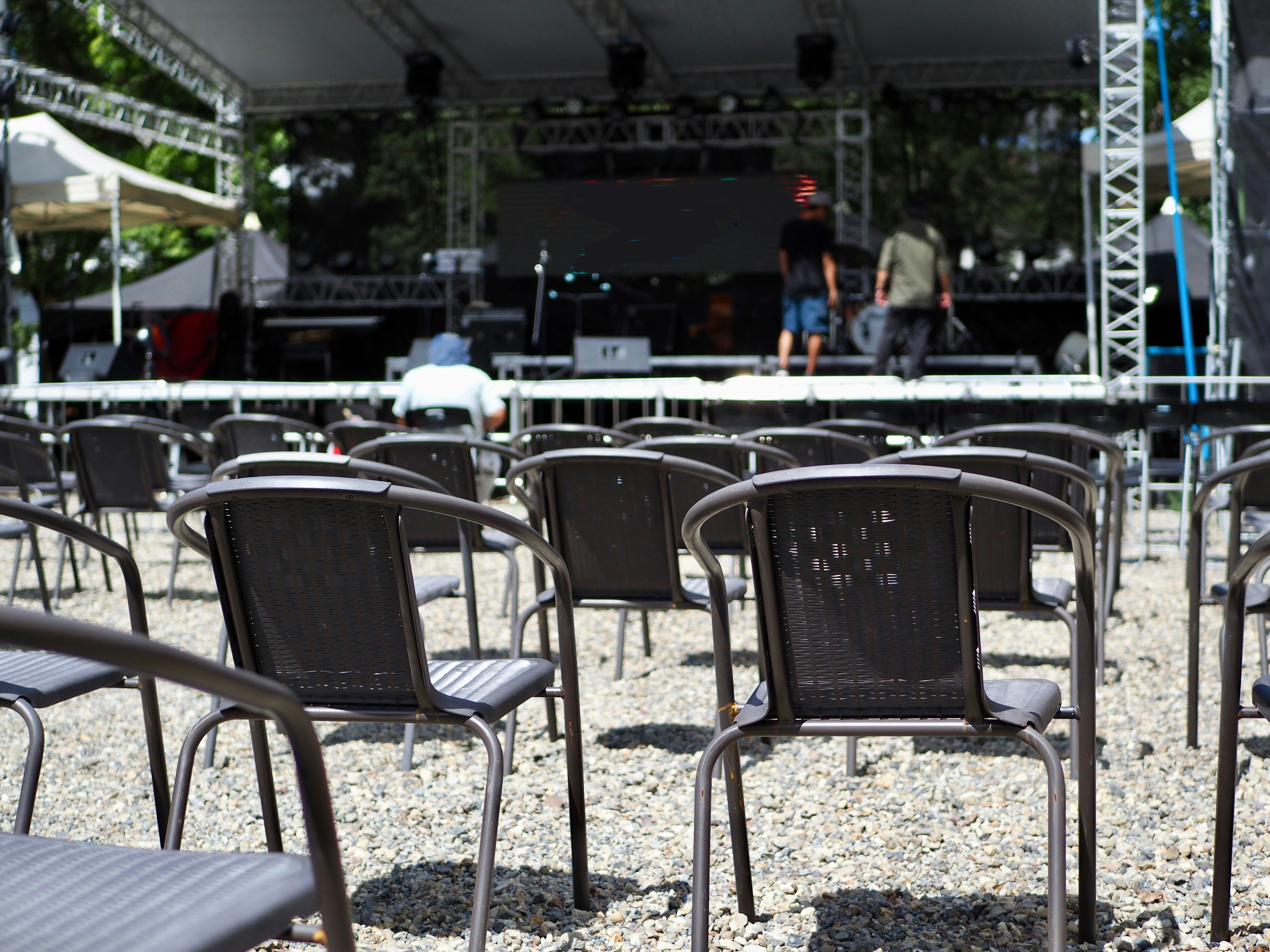 Sillas negras alineadas frente a un escenario con configuración al aire libre