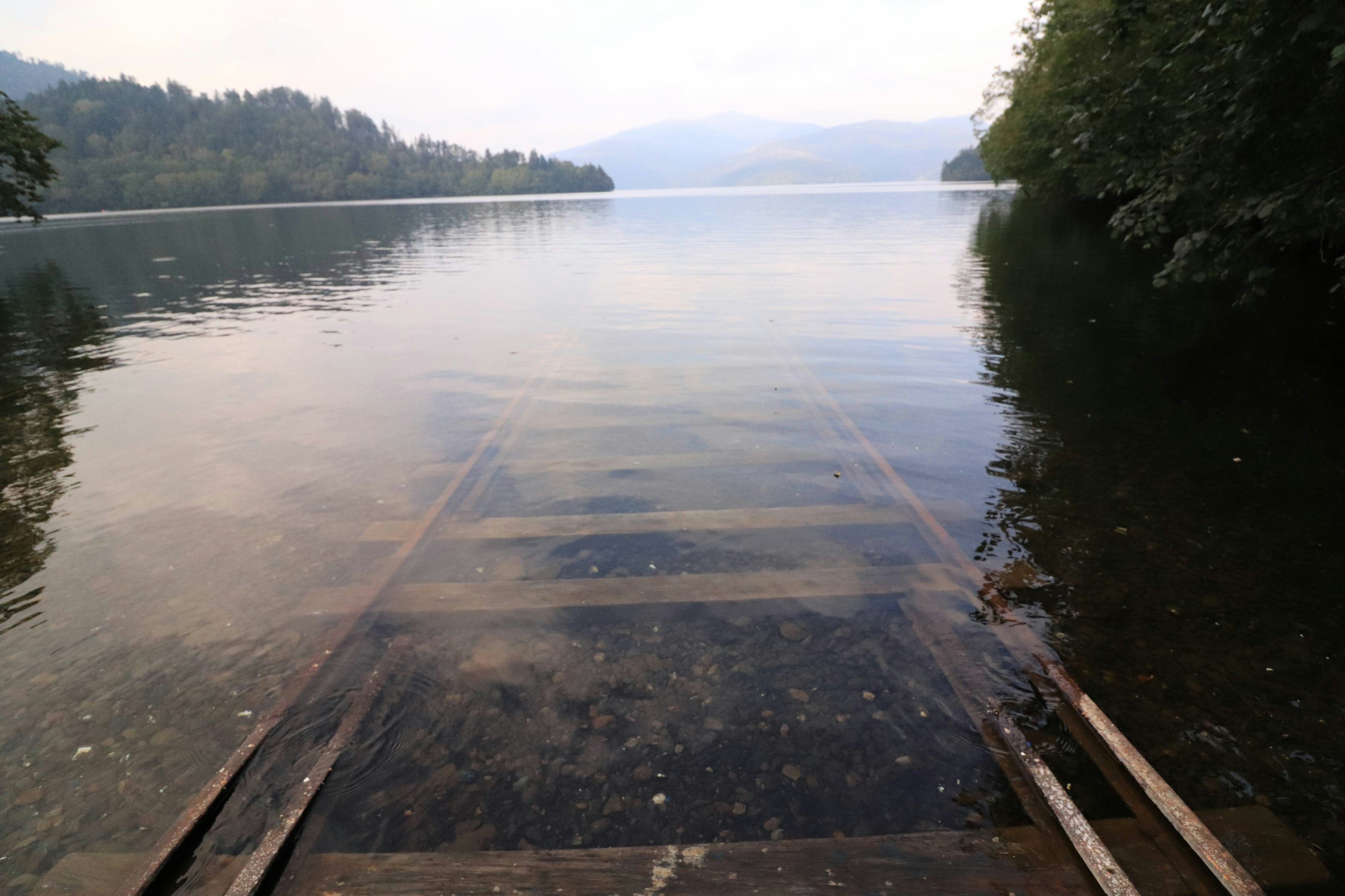 Un quai menant à un lac calme avec des reflets d'arbres sur l'eau