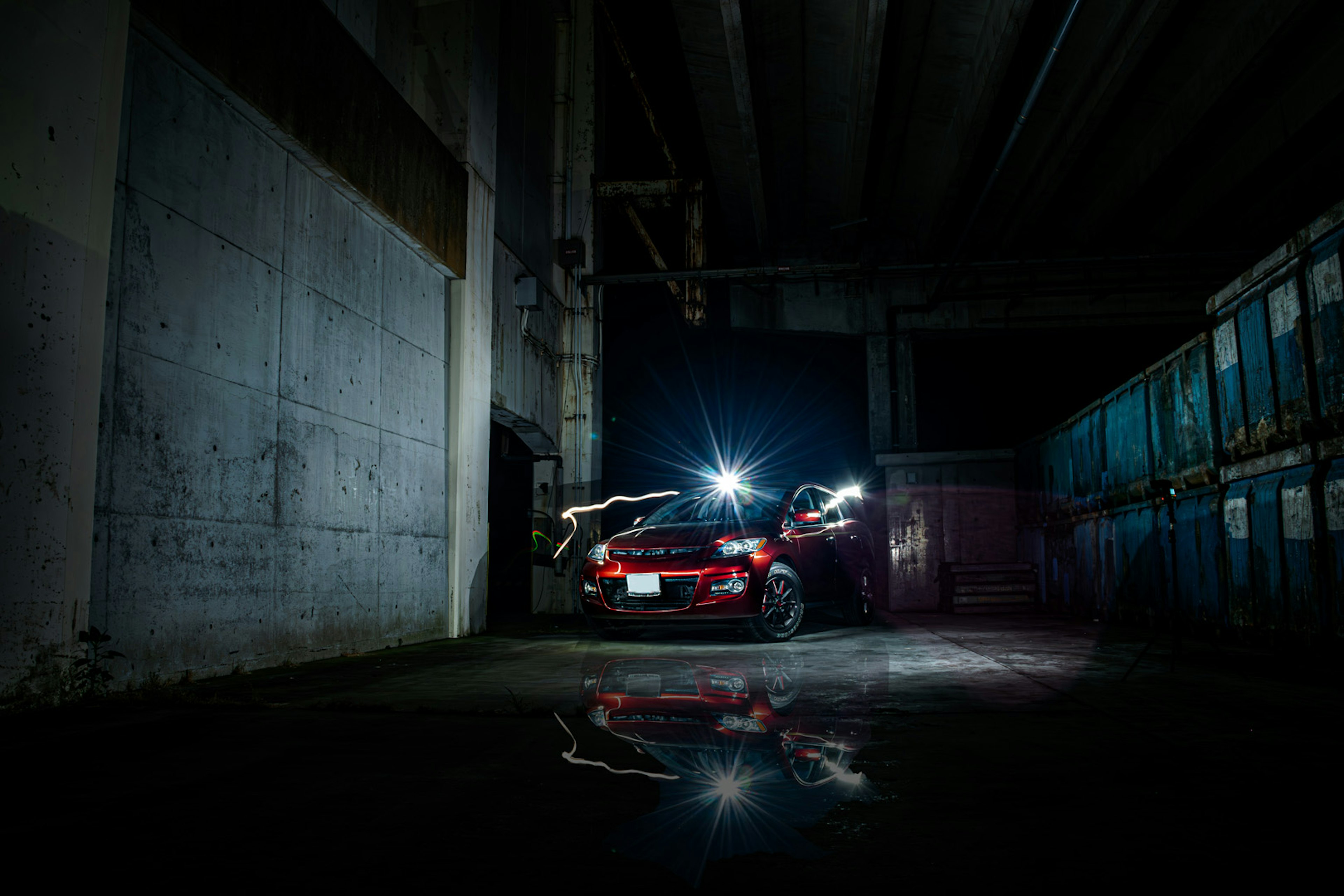 Red car parked in a dark area with blue containers in the background