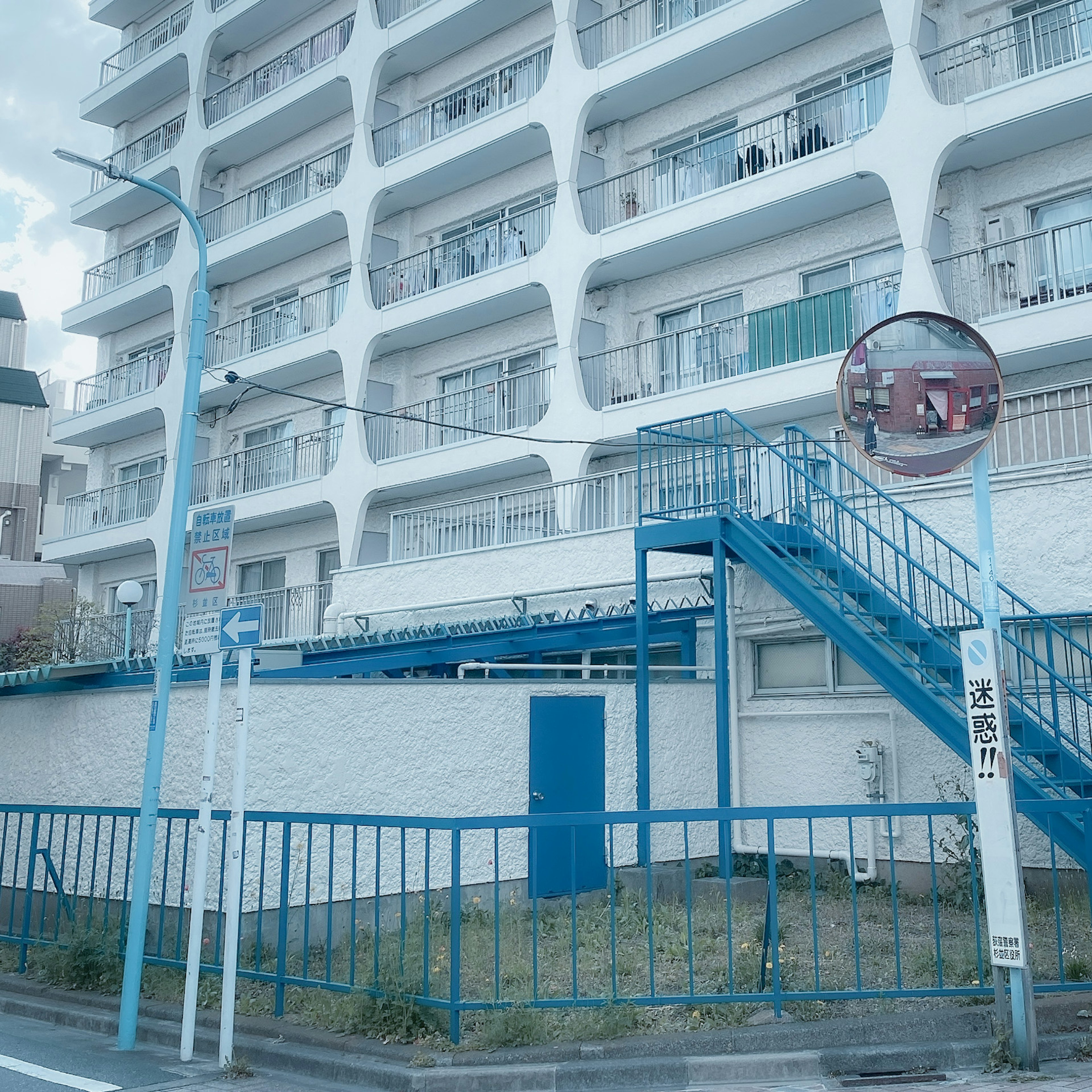 Gedung apartemen putih dengan tangga dan pegangan berwarna biru