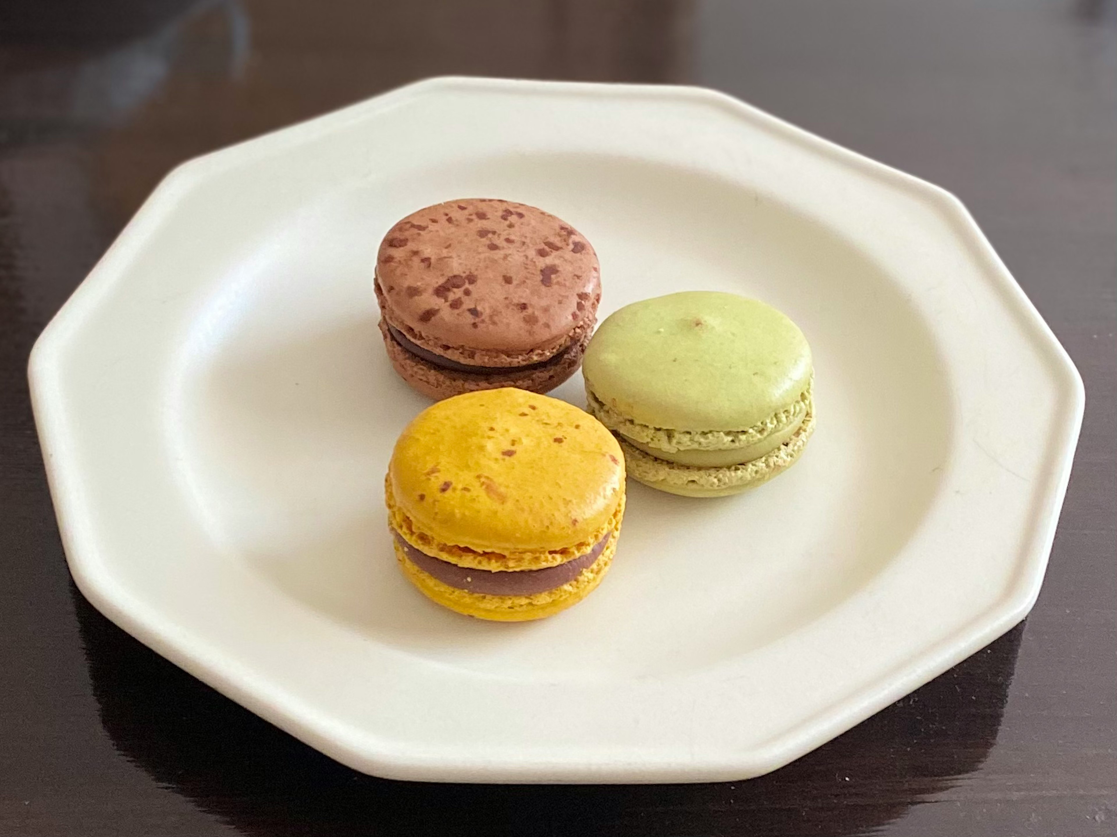 Drei Macarons auf einem weißen Teller gelbes Macaron grünes Macaron braunes Macaron