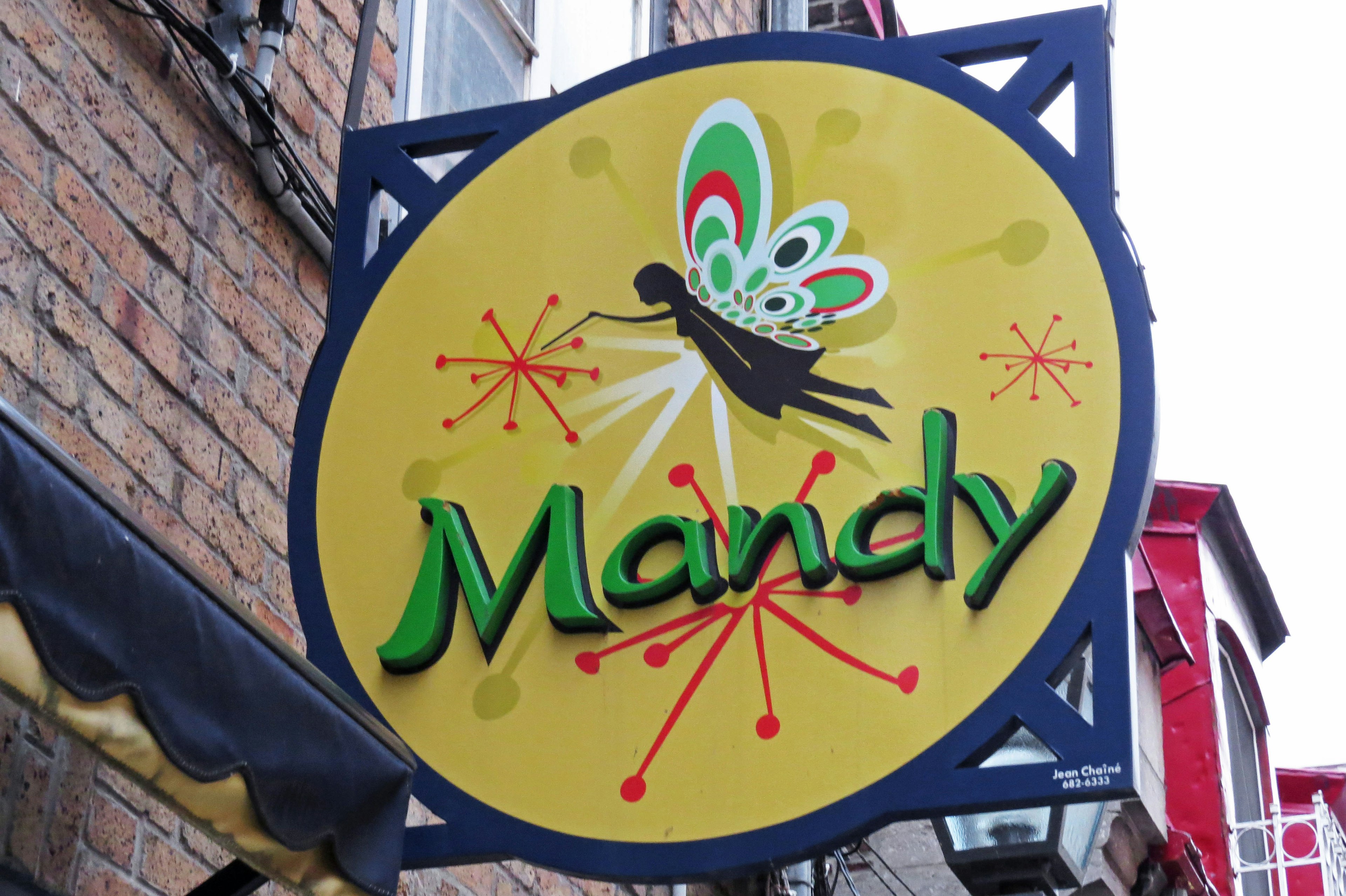 Ein rundes gelbes Schild mit dem Namen 'Mandy' in grünen Buchstaben und einem bunten Schmetterlingsdesign