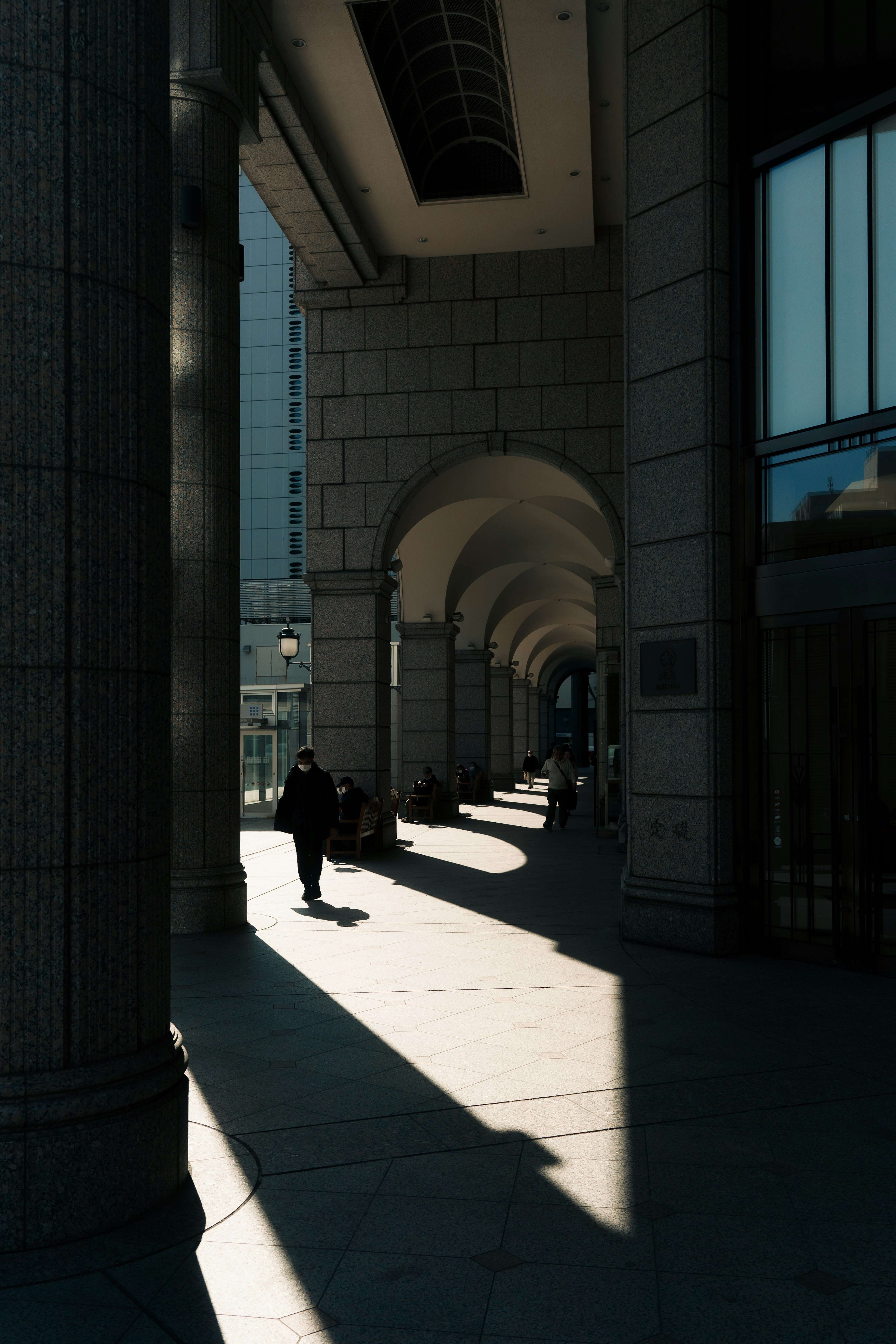 Silhouette einer Person, die durch einen Korridor mit gewölbten Säulen und Schatten geht