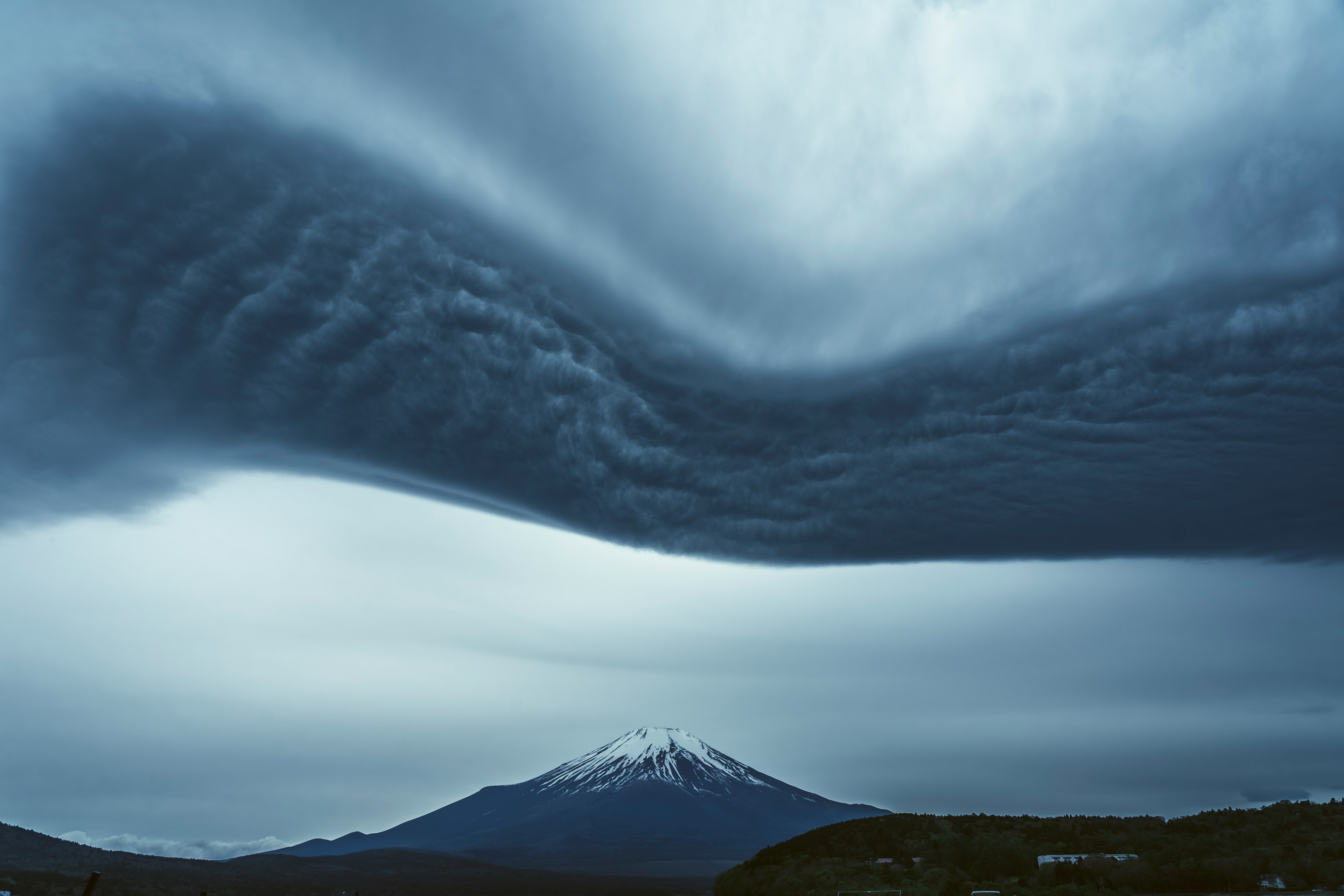 雪をかぶった山と波状の雲が広がる風景