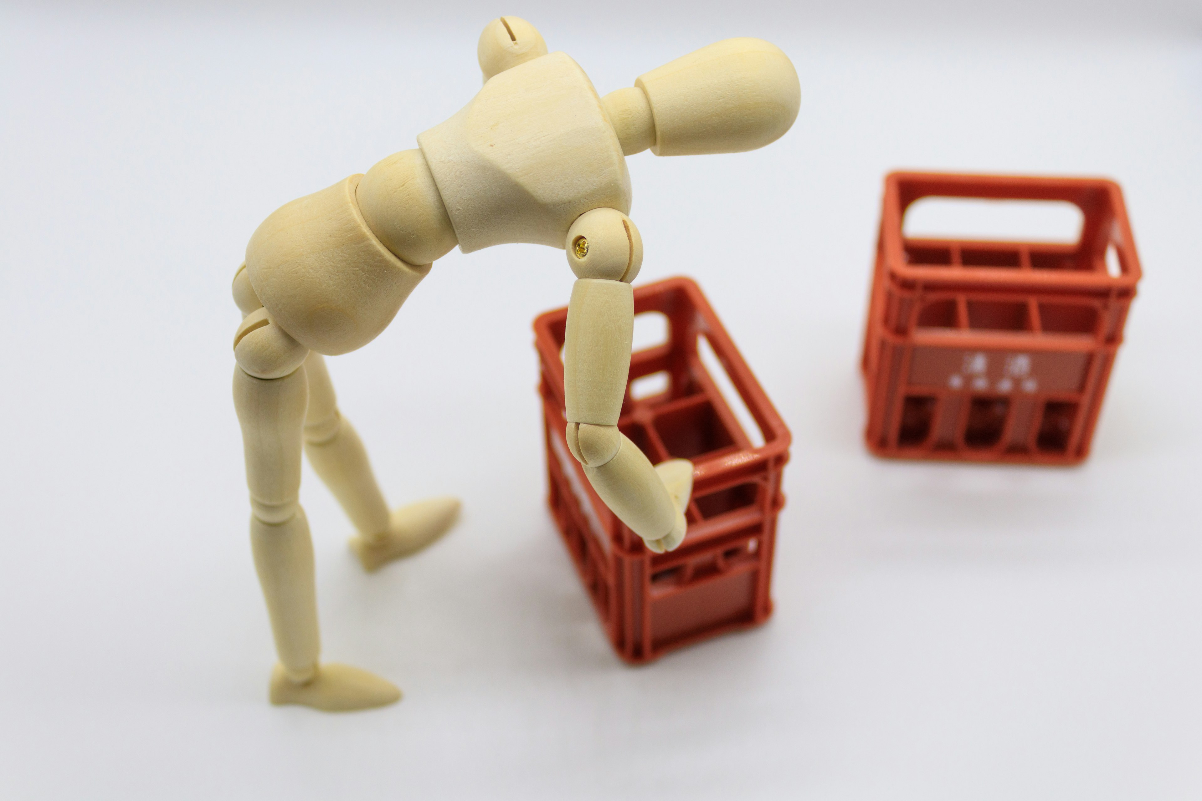 A mannequin bending over to lift a red crate