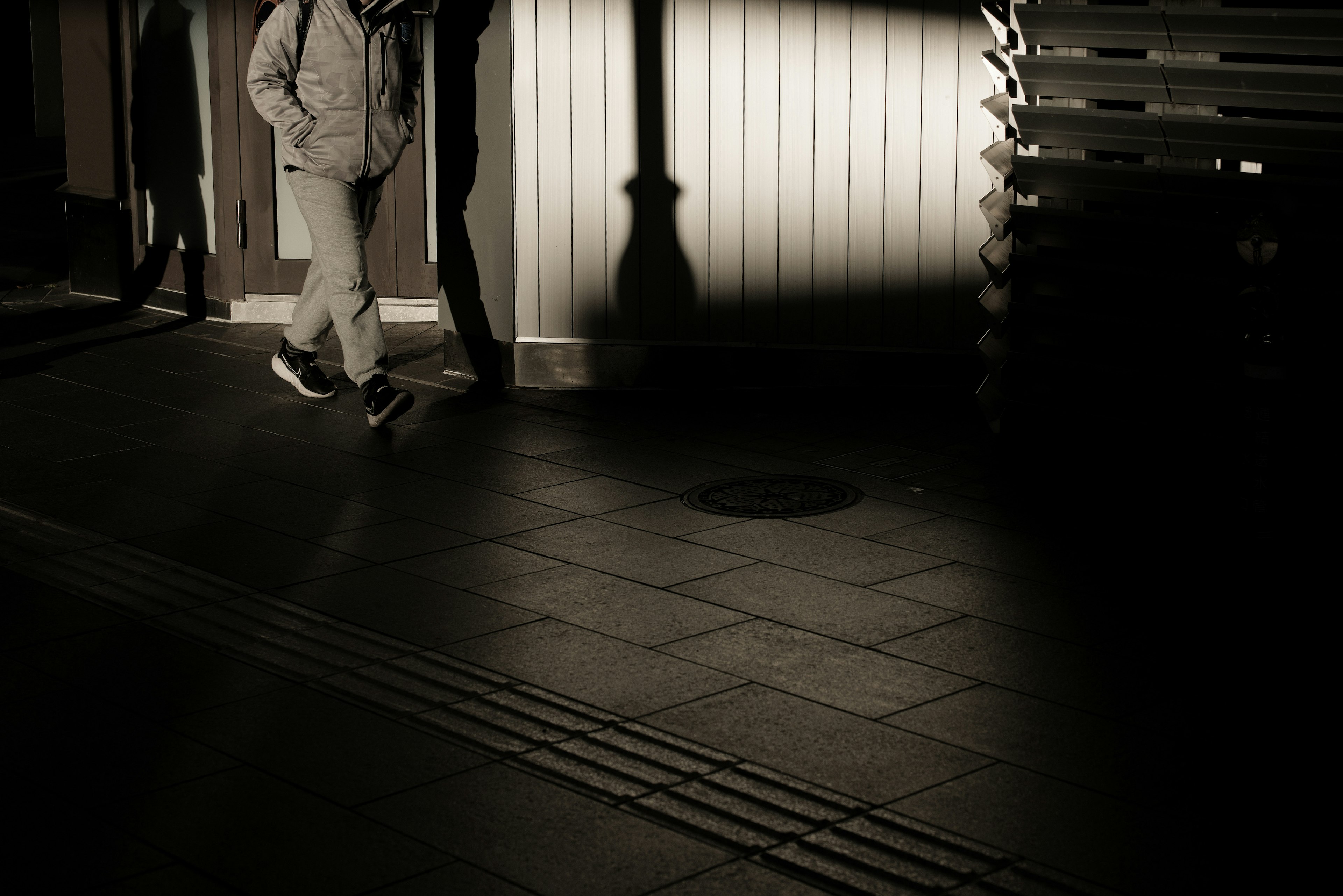 Silhouette of a person walking in a dimly lit street with shadows